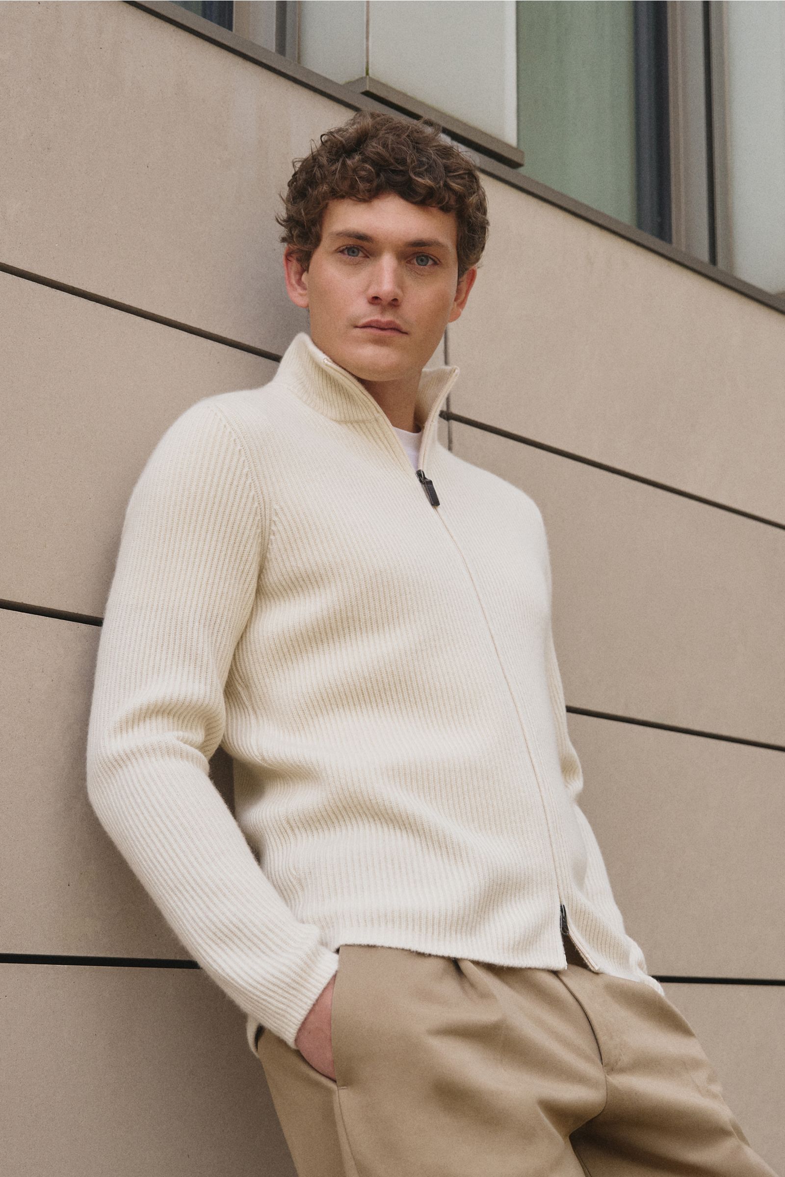 Front view of a man wearing a slim fit von Braun Cashmere cardigan off-white with a high collar and two-way zip, leaning against a beige wall.

Maximum comfort with the highest standards: This cardigan in brioche knit from VON BRAUN’s cashmere collecti