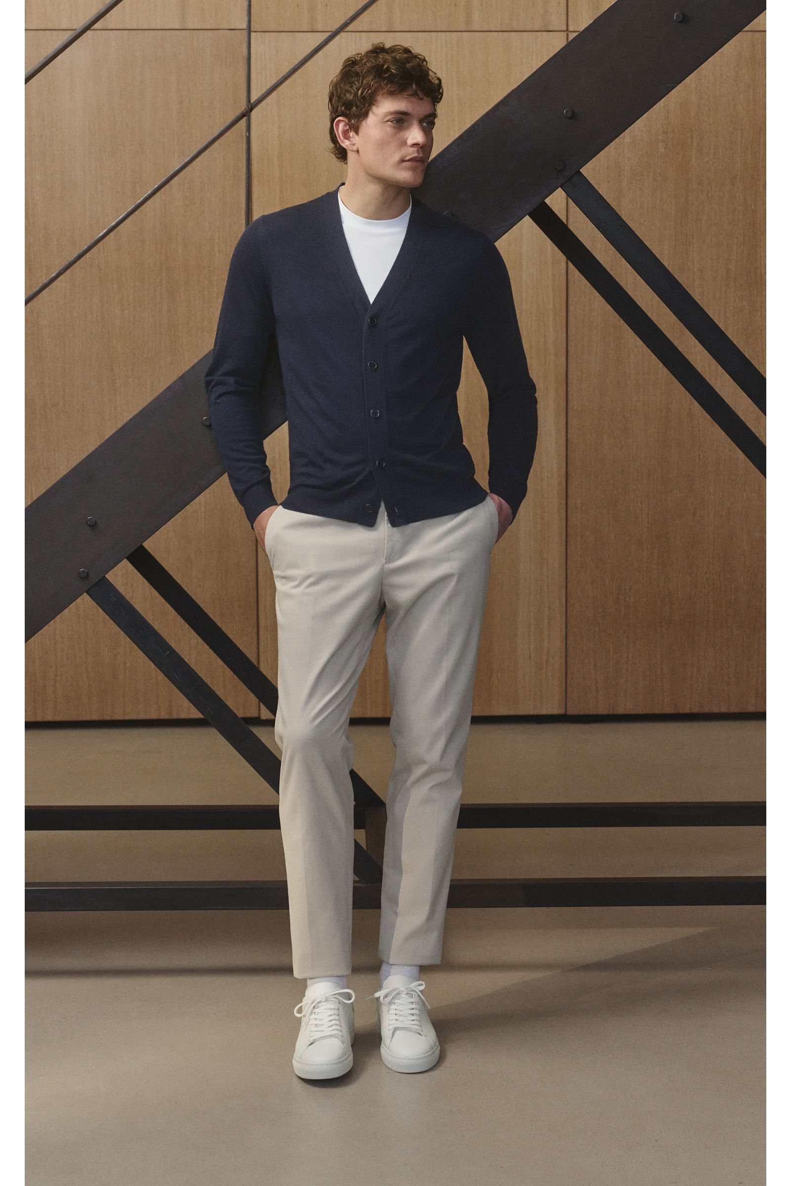 Mann stehend, seitliche Frontansicht, trägt von Braun Merino Cardigan navy aus reiner Merinowolle mit Perlmuttknöpfen, Regular Fit, feines Strickbild, elastische Bündchen.