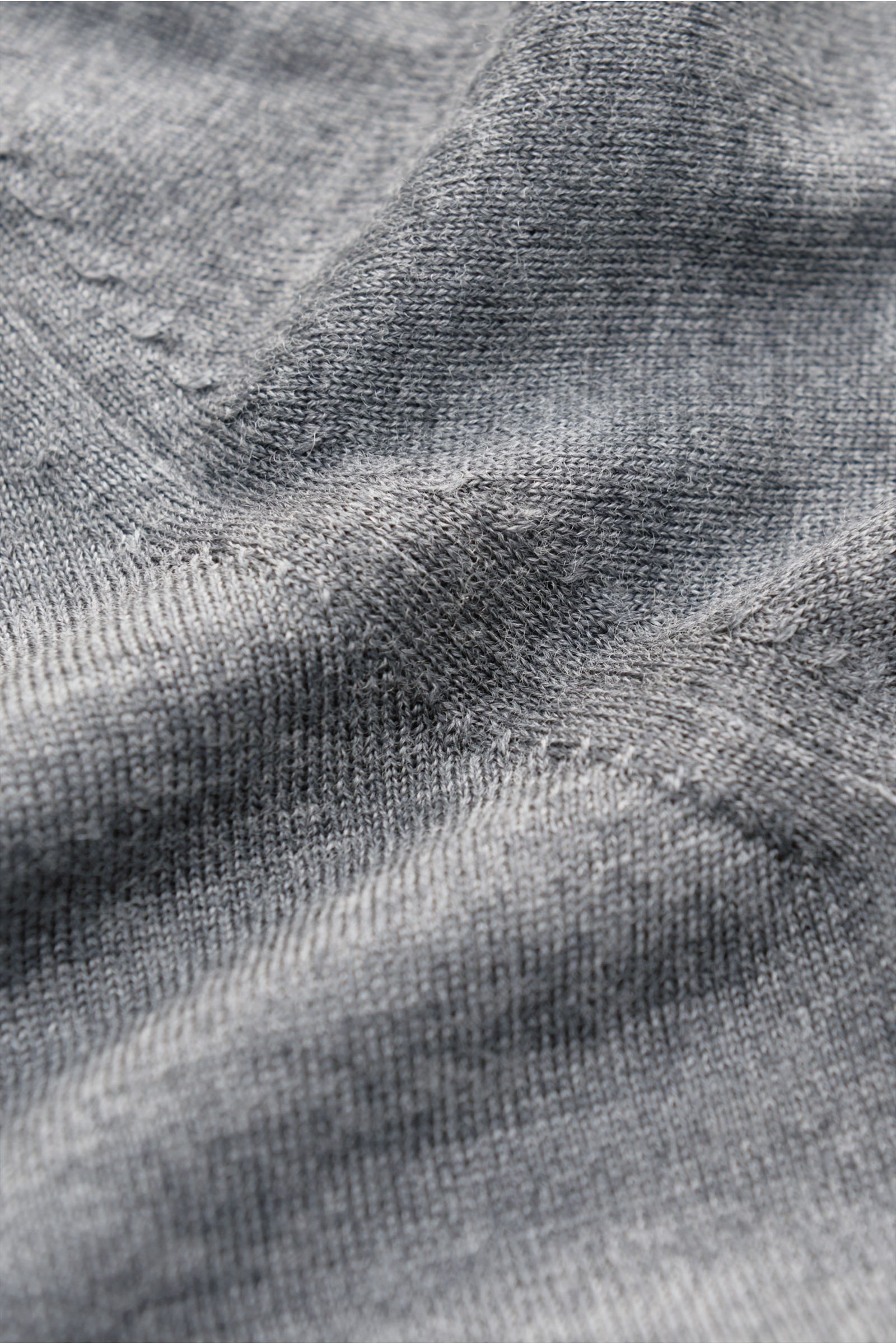 Nahaufnahme des graumelierten von Braun Merino Cardigans aus reiner Merinowolle, feinem Strickbild, weichem Griff, Regular Fit, mit Perlmuttknöpfen und elastischen Rippbündchen, fotografiert aus schräger Perspektive.