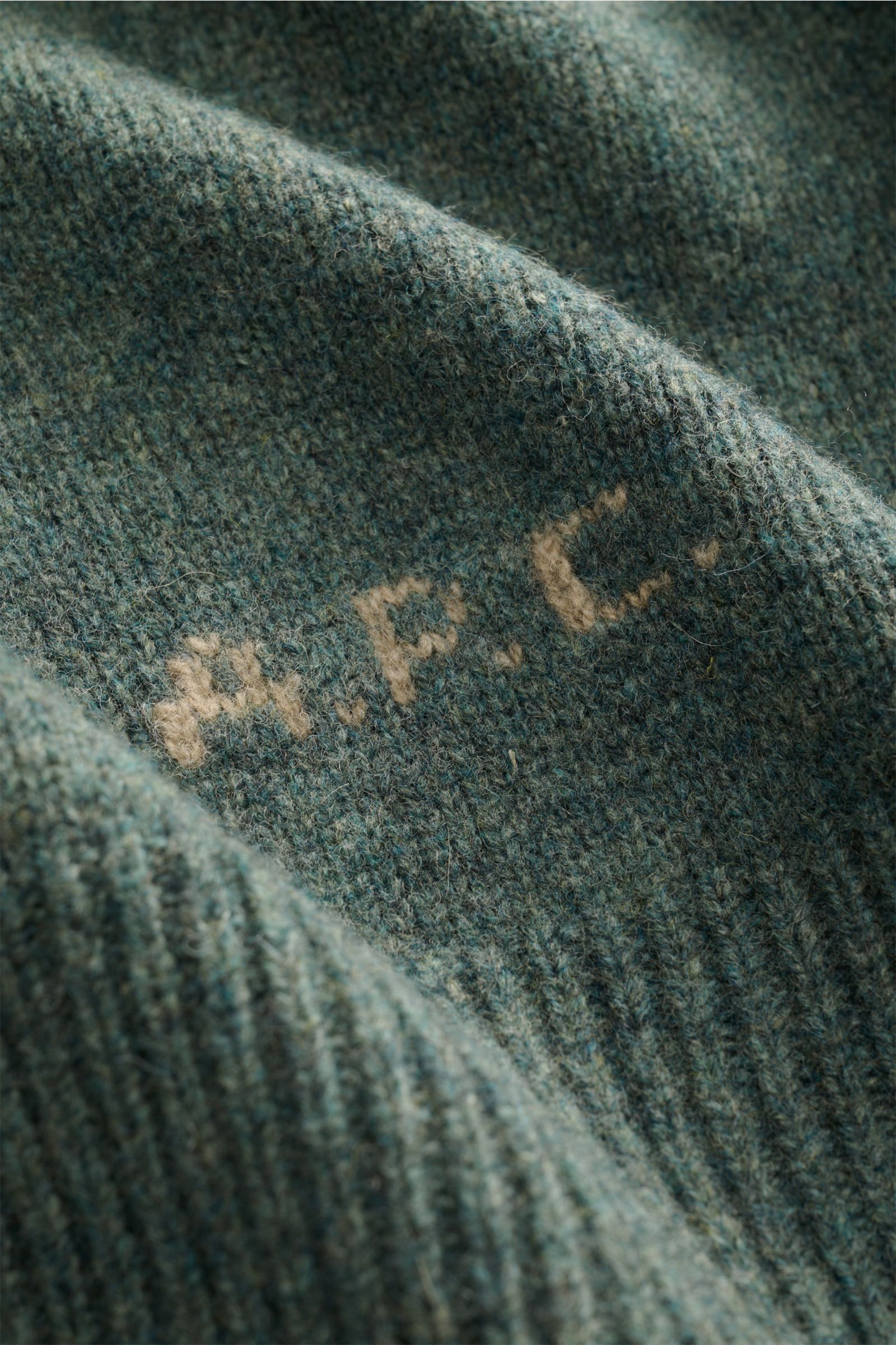 Nahaufnahme des graugrün melierten A.P.C. Cardigans 'Kevin' aus reiner Wolle mit kontrastierendem Logo, Detailtextur aus schräger Perspektive.
