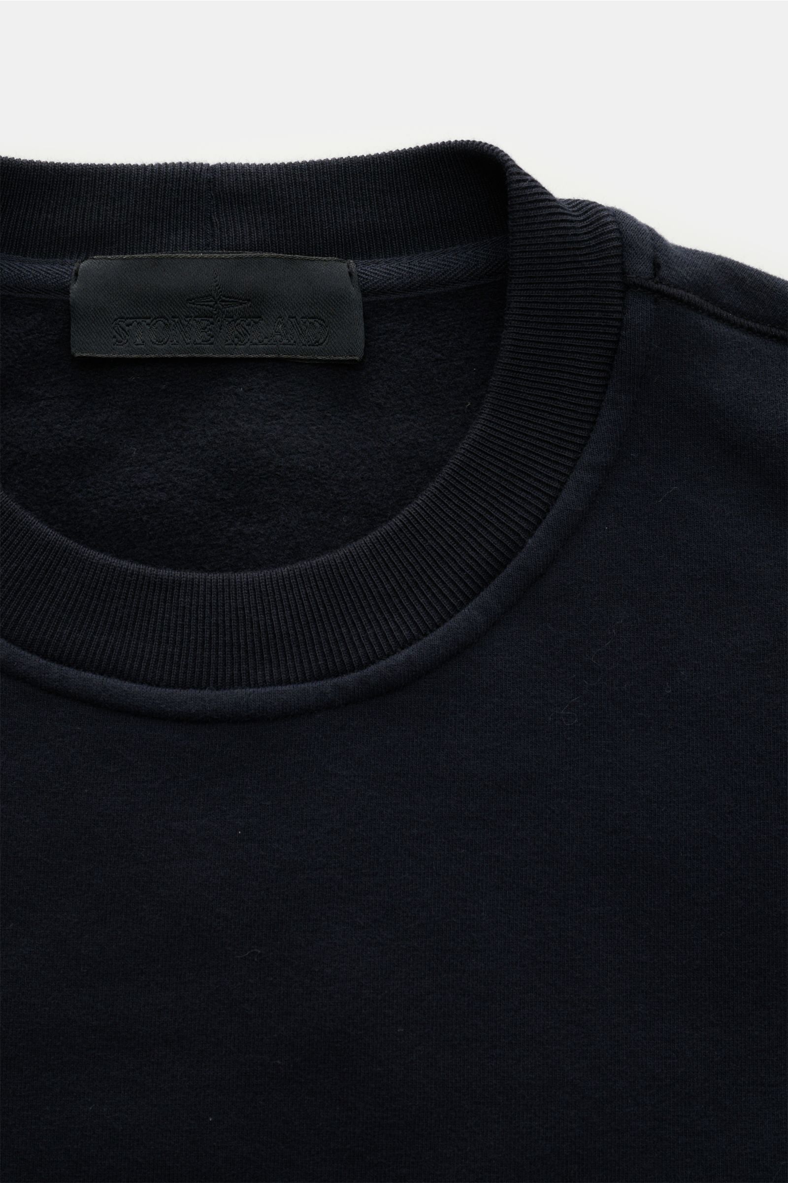 Close-up front-top view of the Stone Island Rundhals-Sweatshirt 'Ghost Piece' navy, showing the ribbed round neckline and the black Stone Island label inside the collar. Softer, innen angerauter Baumwoll-Sweat bildet die Basis für dieses legere Sweatsh