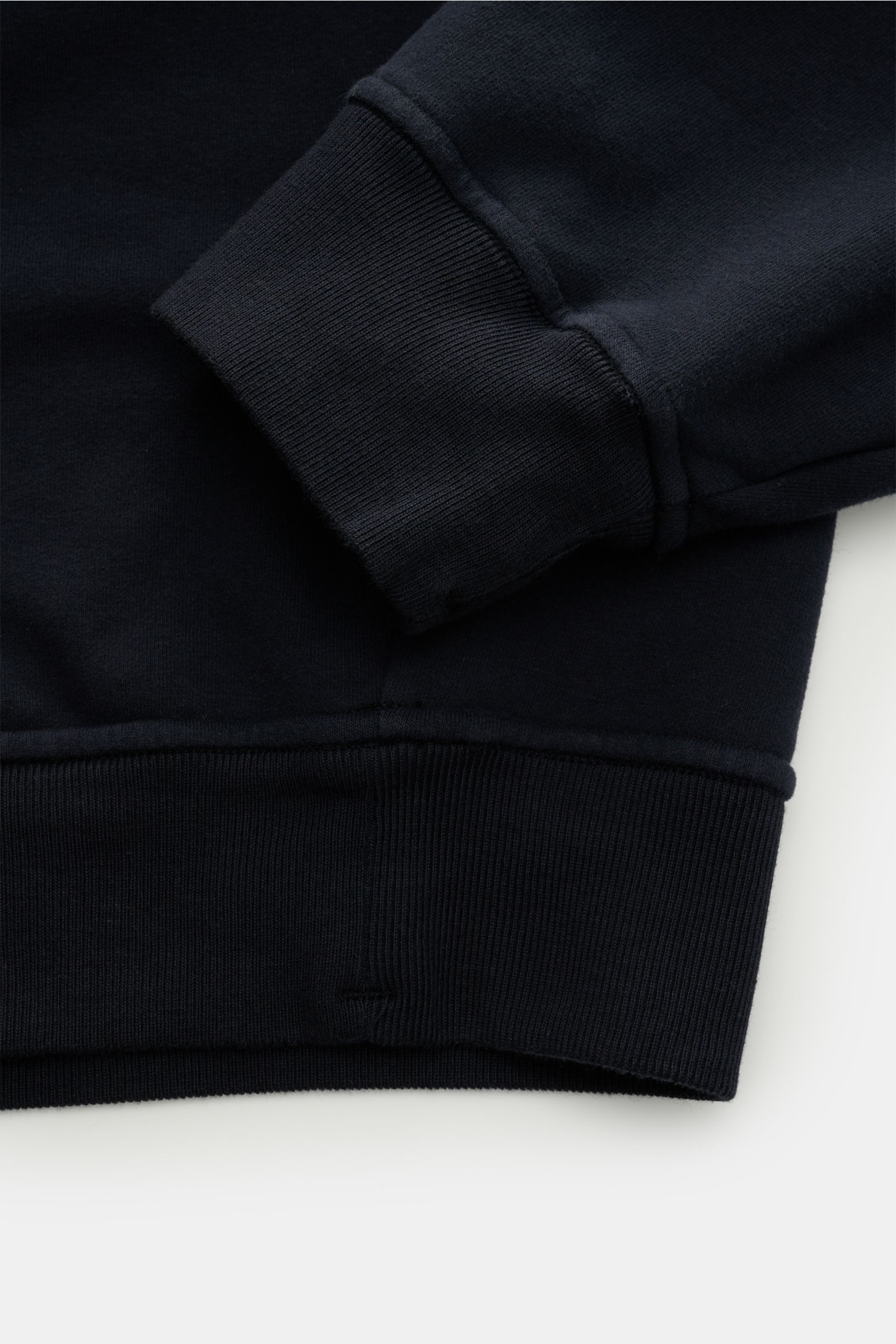 Close-up image of the cuff and hem of the Stone Island Rundhals-Sweatshirt 'Ghost Piece' navy, showing the soft, garment-dyed, elastic cotton fabric with comfortable ribbed cuffs and a tonal compass badge, photographed from a top-down perspective. 

So