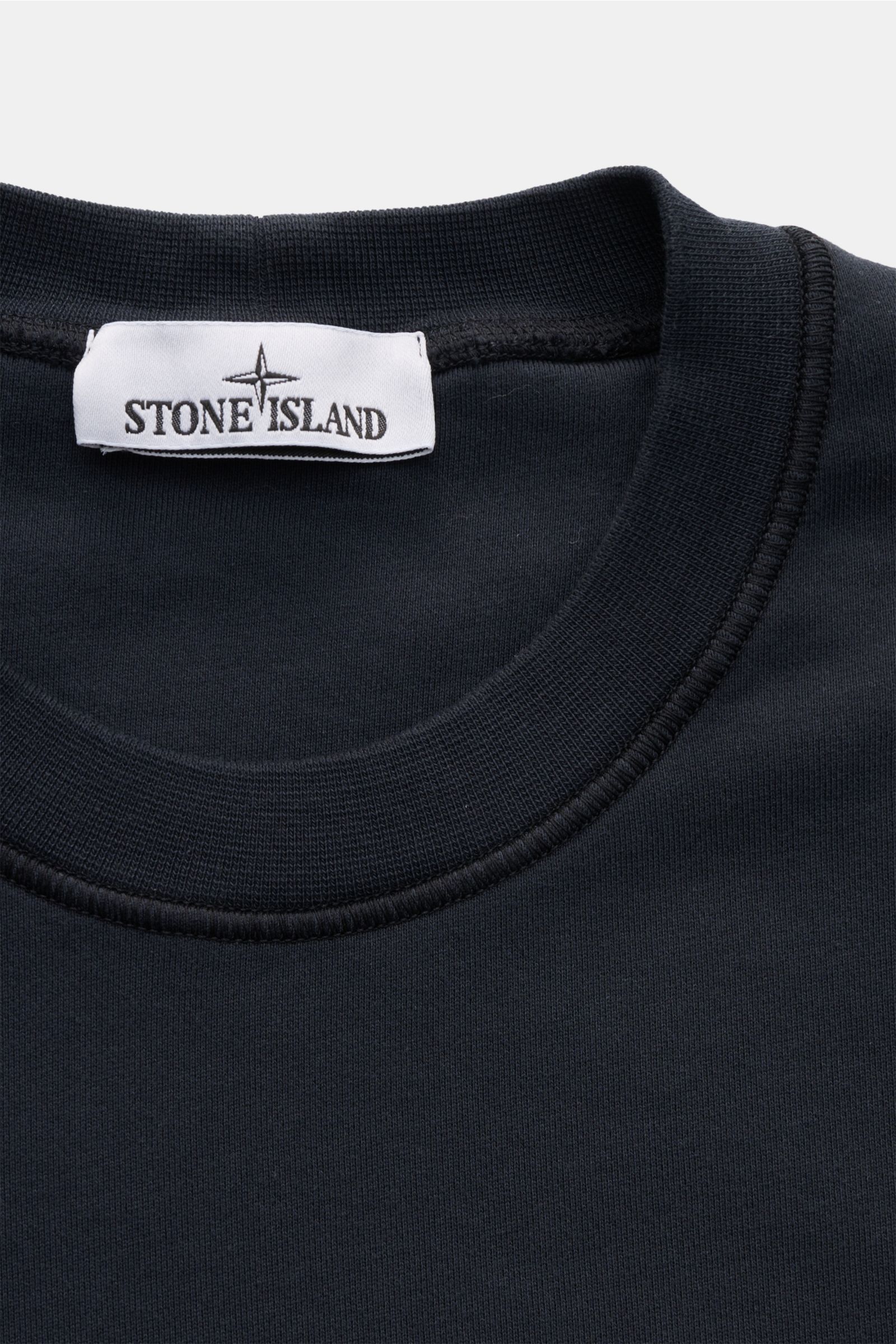 Nahaufnahme von Stone Island Rundhals-Sweatshirt navy, slim fit, garment dyed aus weicher Baumwolle mit Rippkragen, Label innen am Hals.