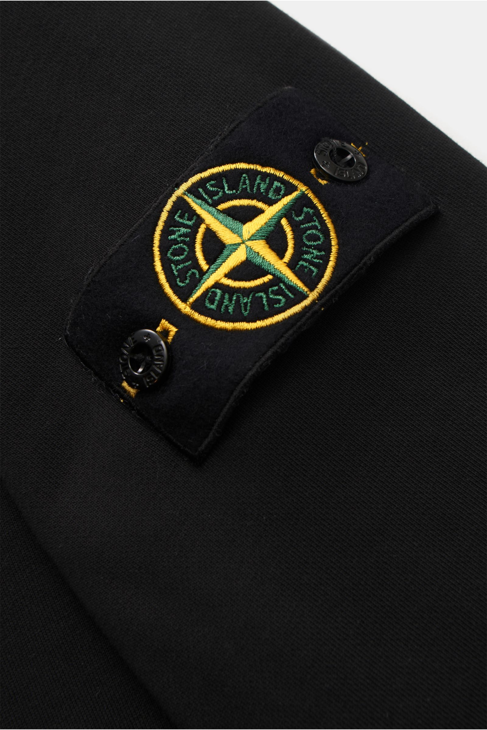 Stone Island Rundhals-Sweatshirt schwarz in Nahaufnahme, Detail des schwarzen Kompass-Badges am Ärmel aus weicher, garment dyed Baumwolle.