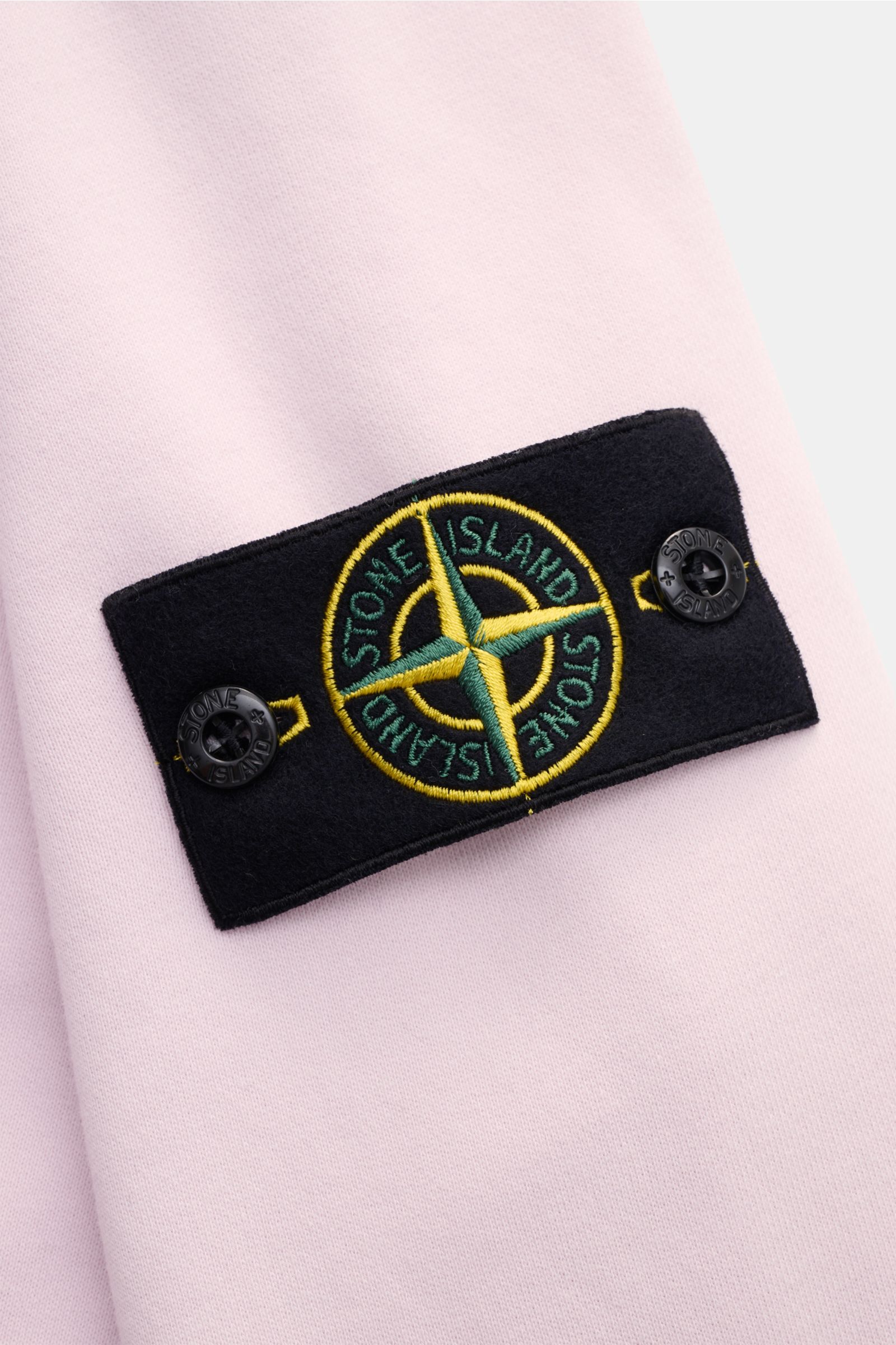 Nahaufnahme des Stone Island Rundhals-Sweatshirts rosé von der Ärmelperspektive mit typischem Kompass-Badge, weichem Griff, Slim Fit, Rundhalsausschnitt, markanter Nahtverarbeitung, garment dyed, reiner Baumwolle und komfortablen Rippbündchen.