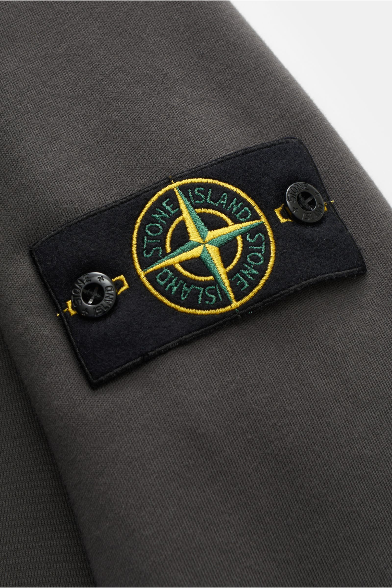 Stone Island Rundhals-Sweatshirt dunkelgrau, Nahaufnahme von Ärmel mit typischem Kompass-Badge, Sweat aus reiner Baumwolle, weicher Griff, markante Nahtverarbeitung, garment dyed, Slim Fit, Rundhalsausschnitt, Sweat Innenseite, komfortable Rippbündchen.