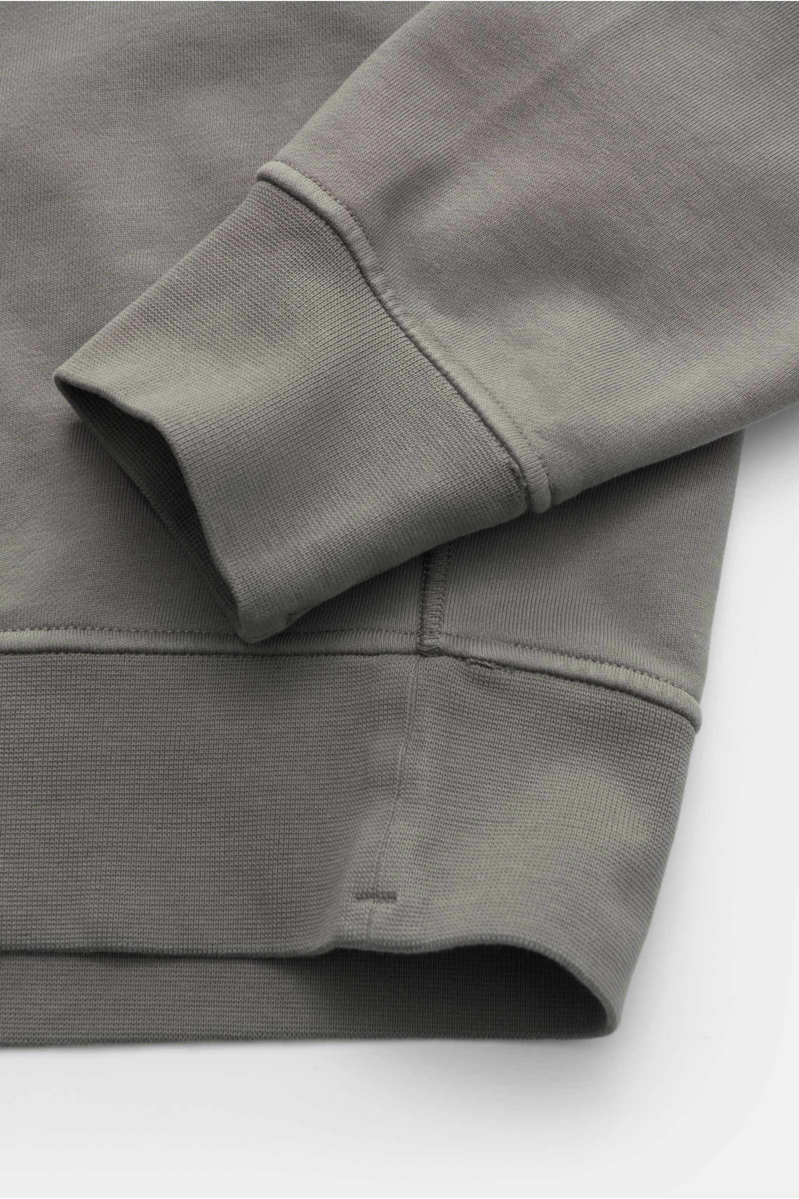 Nahaufnahme des Stone Island Rundhals-Sweatshirts grau, Vorderseite schräg von oben, Sweat aus reiner Baumwolle, weicher Griff, markante Nahtverarbeitung, garment dyed, Regular Fit, Rundhalsausschnitt, typisches Kompass-Badge, softe Innenseite, komfortabl