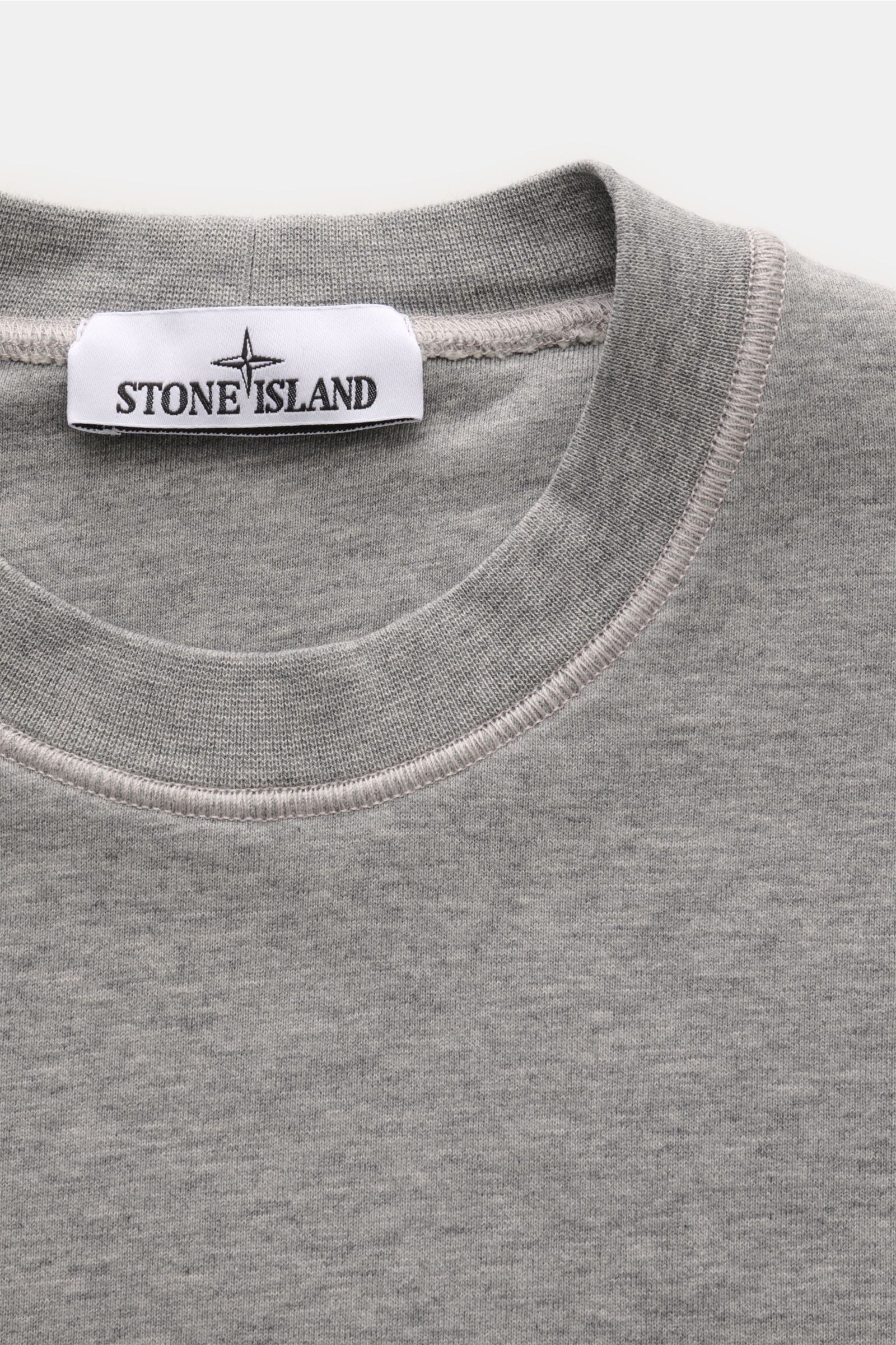 Stone Island Rundhals-Sweatshirt grau meliert, Nahaufnahme von oben, Sweat aus reiner Baumwolle, weicher Griff, markante Nahtverarbeitung, garment dyed, Slim Fit, Rundhalsausschnitt, typisches Kompass-Badge, komfortable Rippbündchen.