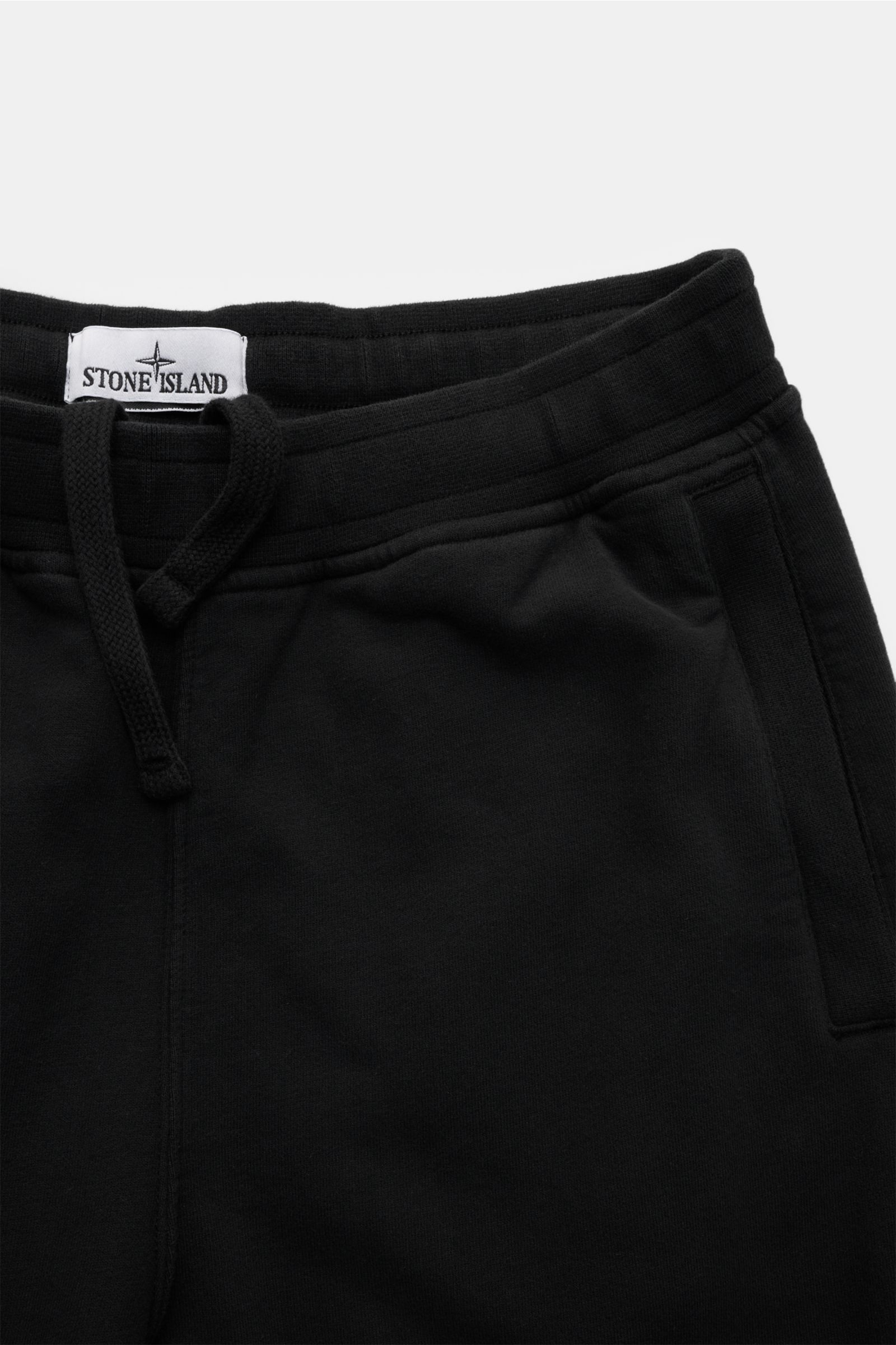 Nahe Aufnahme von Stone Island Sweathose schwarz mit elastischem Bund, Tunnelzug, schräge Leistentaschen und labeltypischem Kompass-Badge, aus reiner Baumwolle, weicher Griff, garment dyed, Tapered Fit, reguläre Oberschenkelweite, knöchellang, sehr schmal