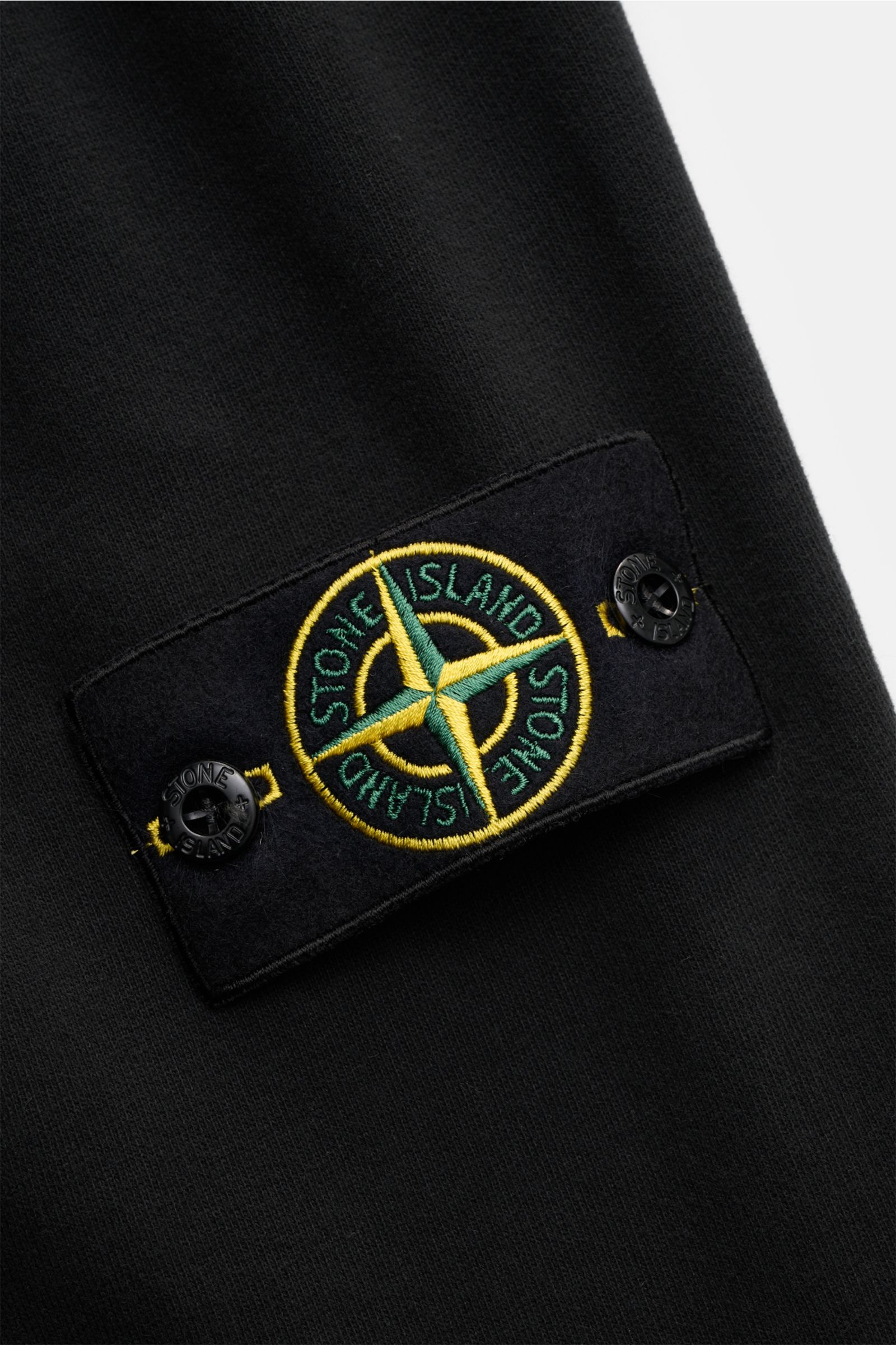 Nahaufnahme des labeltypischen Kompass-Badges auf der Stone Island Sweathose schwarz, gefertigt aus weichem, garment dyed Baumwoll-Sweat mit elastischem Bund, schmal zulaufend, knöchellang und mit Rippbündchen.