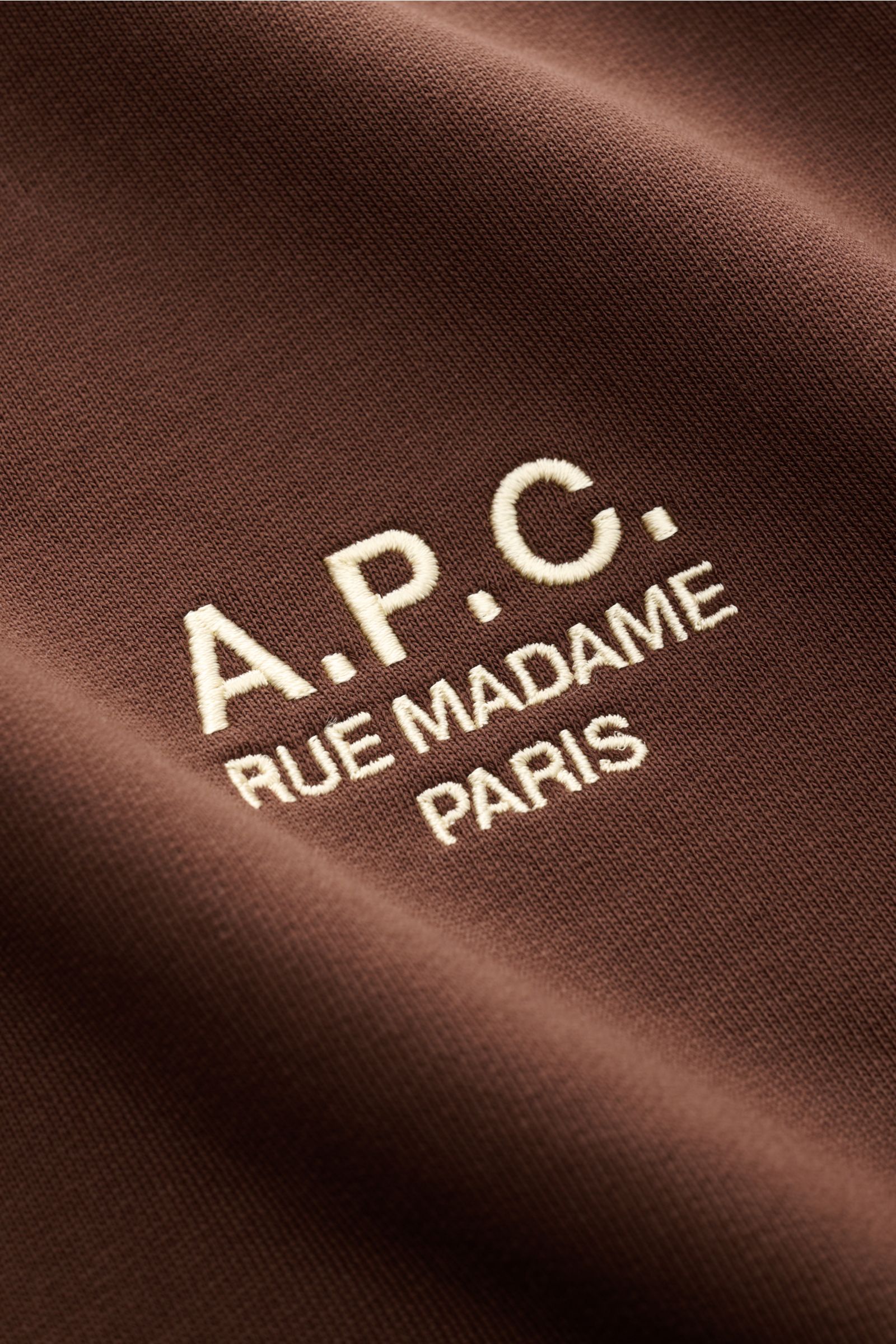 Nahaufnahme des A.P.C. Rundhals-Sweatshirts 'Standard Rue Madame' braun mit farblich abgesetztem Logo-Stitching auf der Brust, fotografiert aus schräger Perspektive. Streetwear mit französischem Flair, aus leicht elastischer Baumwolle, weicher Griff, Slim
