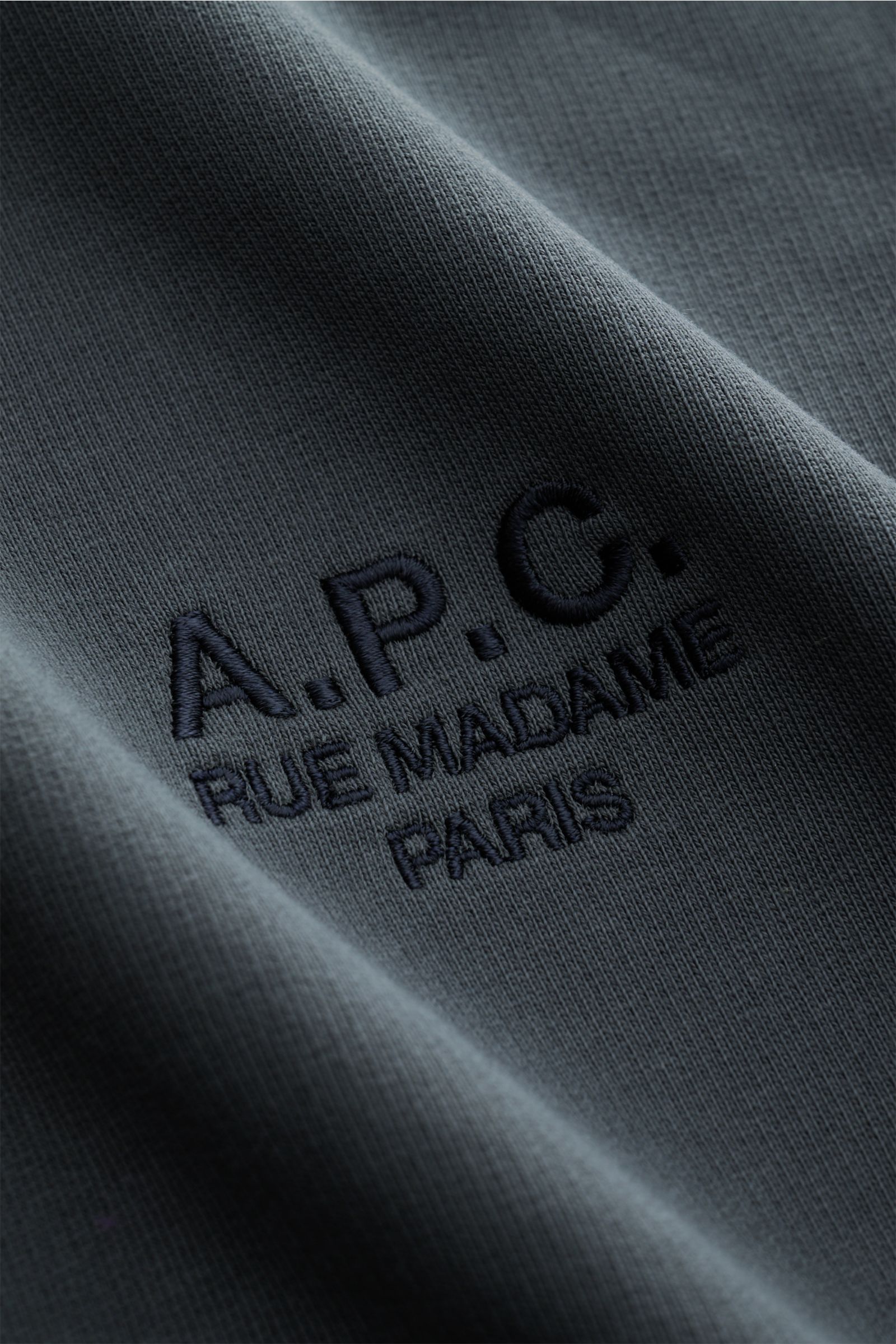 Close-up view of the dark gray A.P.C. Rundhals-Sweatshirt 'Standard Rue Madame' showing the color-contrasting stitched logo on soft, slightly elastic cotton fabric.

Streetwear mit französischem Flair: Das minimalistische Sweatshirt 'Standard Rue Madam