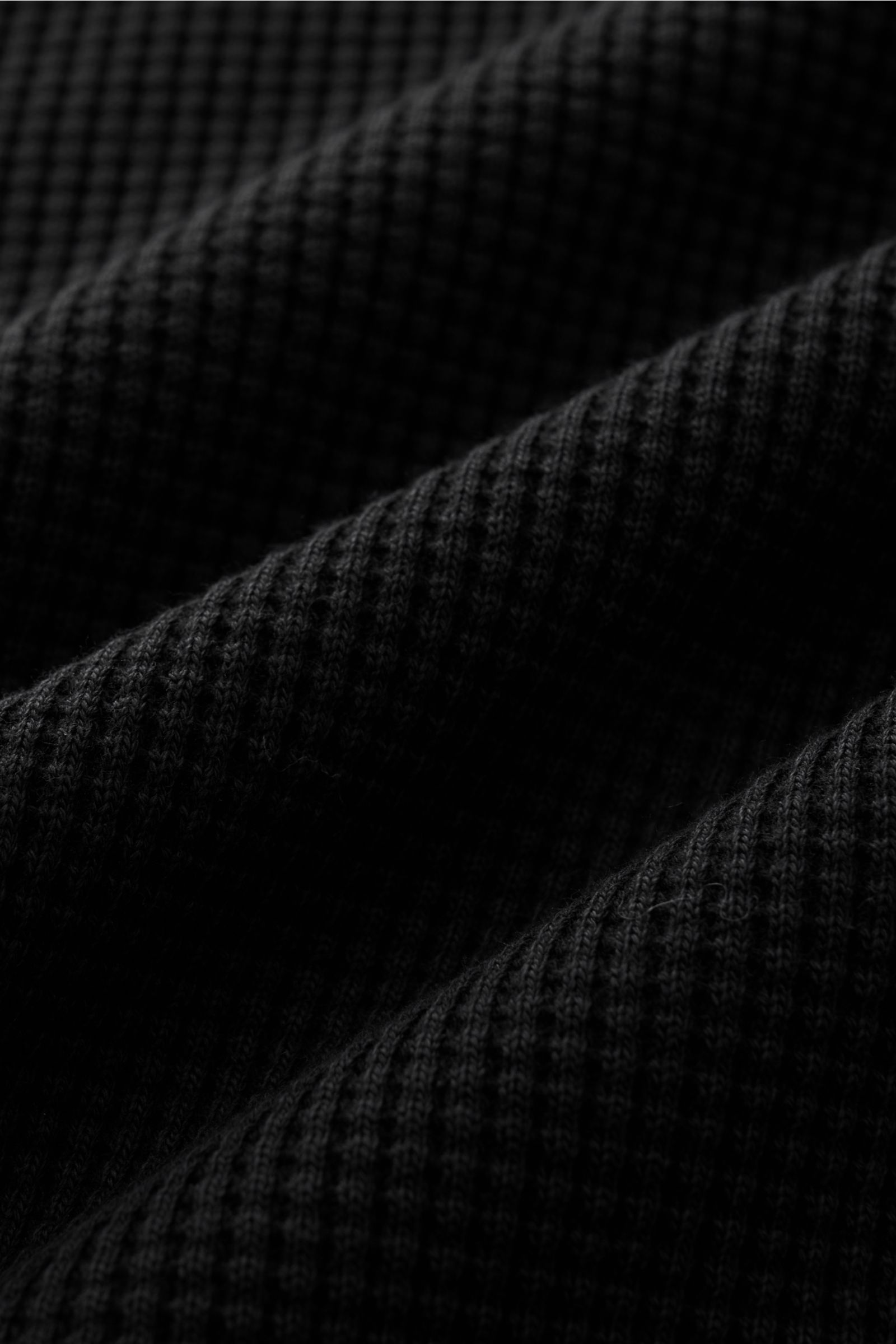 Stone Island Rundhalspullover 'Waffle' schwarz im Nahaufnahme-Waffelstrick aus reiner Baumwolle mit leichter Haptik, Perspektive von oben.