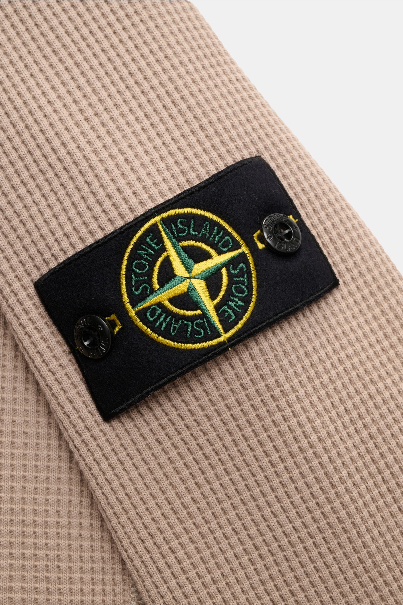 Stone Island Rundhalspullover 'Waffle' taupe shown in close-up from a side angle, highlighting the waffle-knit cotton fabric and the black compass badge on the upper arm. Basic Piece mit Twist: Dieser Pullover im Waffelstrick von STONE ISLAND wird zur 