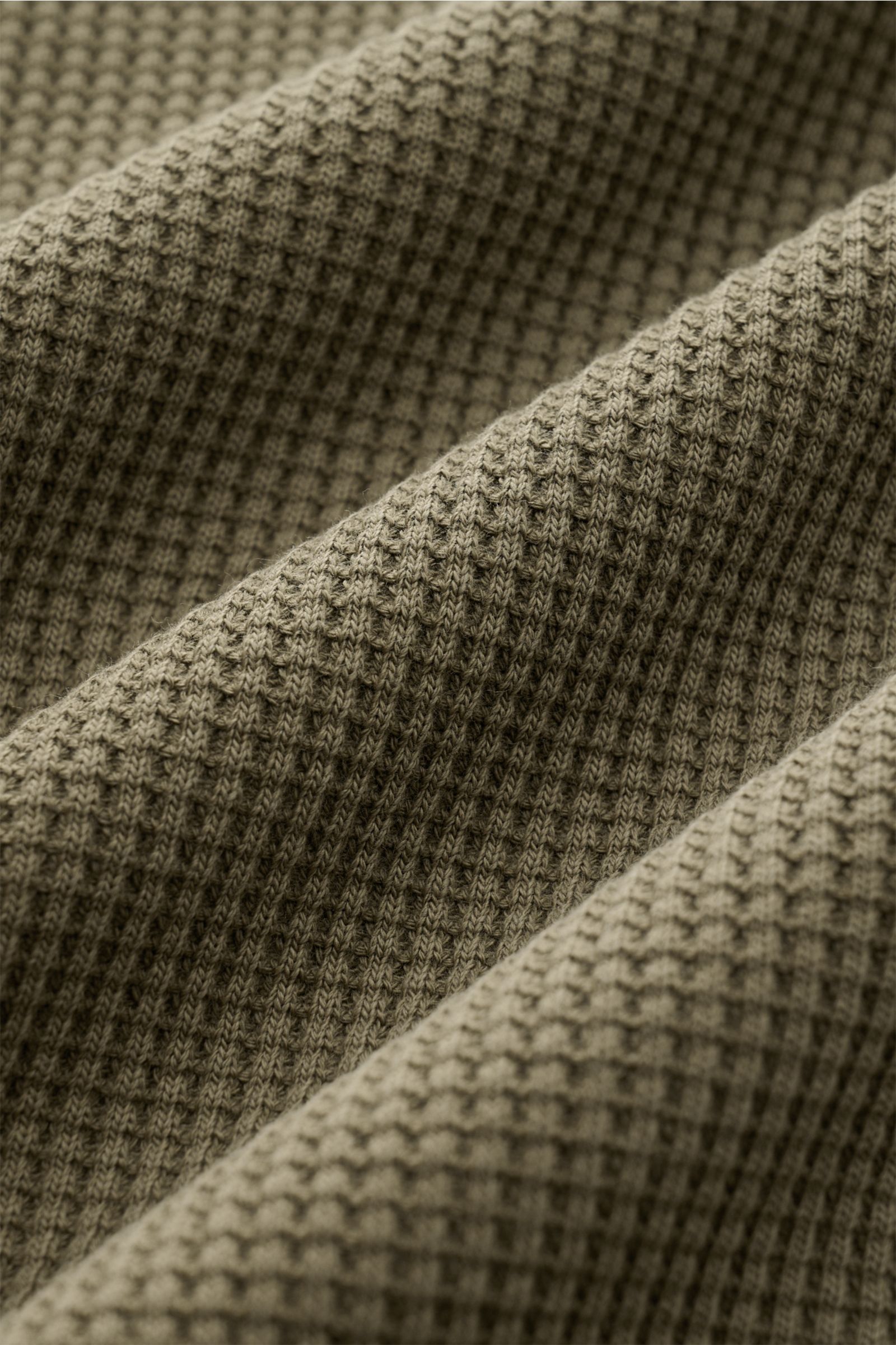 Close-up, angled view of the olive green Stone Island Rundhalspullover 'Waffle' showing detailed waffle knit texture. Basic Piece mit Twist: Dieser Pullover im Waffelstrick von STONE ISLAND wird zur idealen Grundlage moderner Freizeitlooks und lässt si