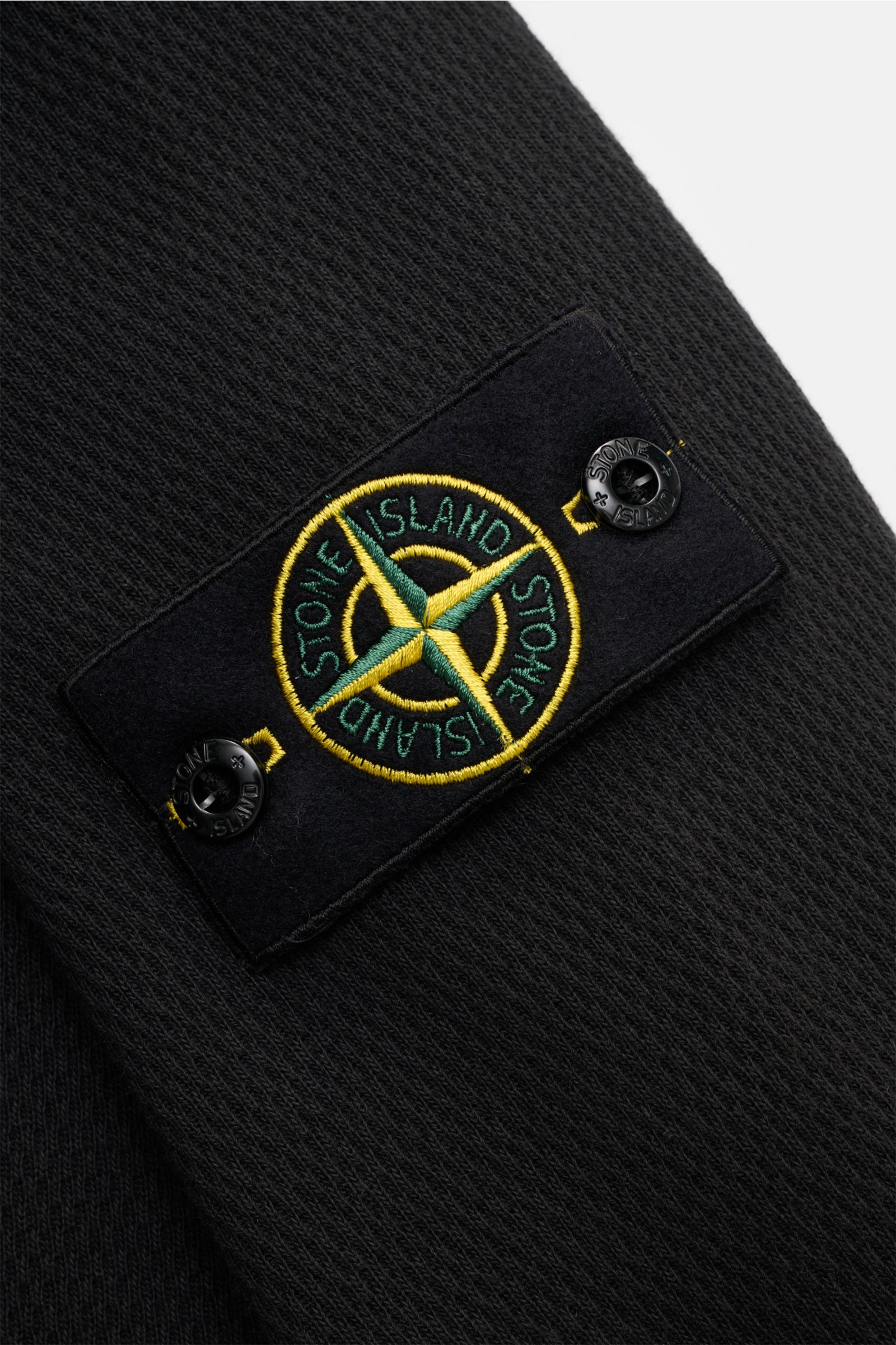 Stone Island Rundhalspullover schwarz Nahaufnahme des Kompass-Badges am Oberarm, strukturierte Jersey-Qualität aus reiner Baumwolle, feines Strickbild, markante Overlock-Nähte, elastische Bündchen sichtbar.