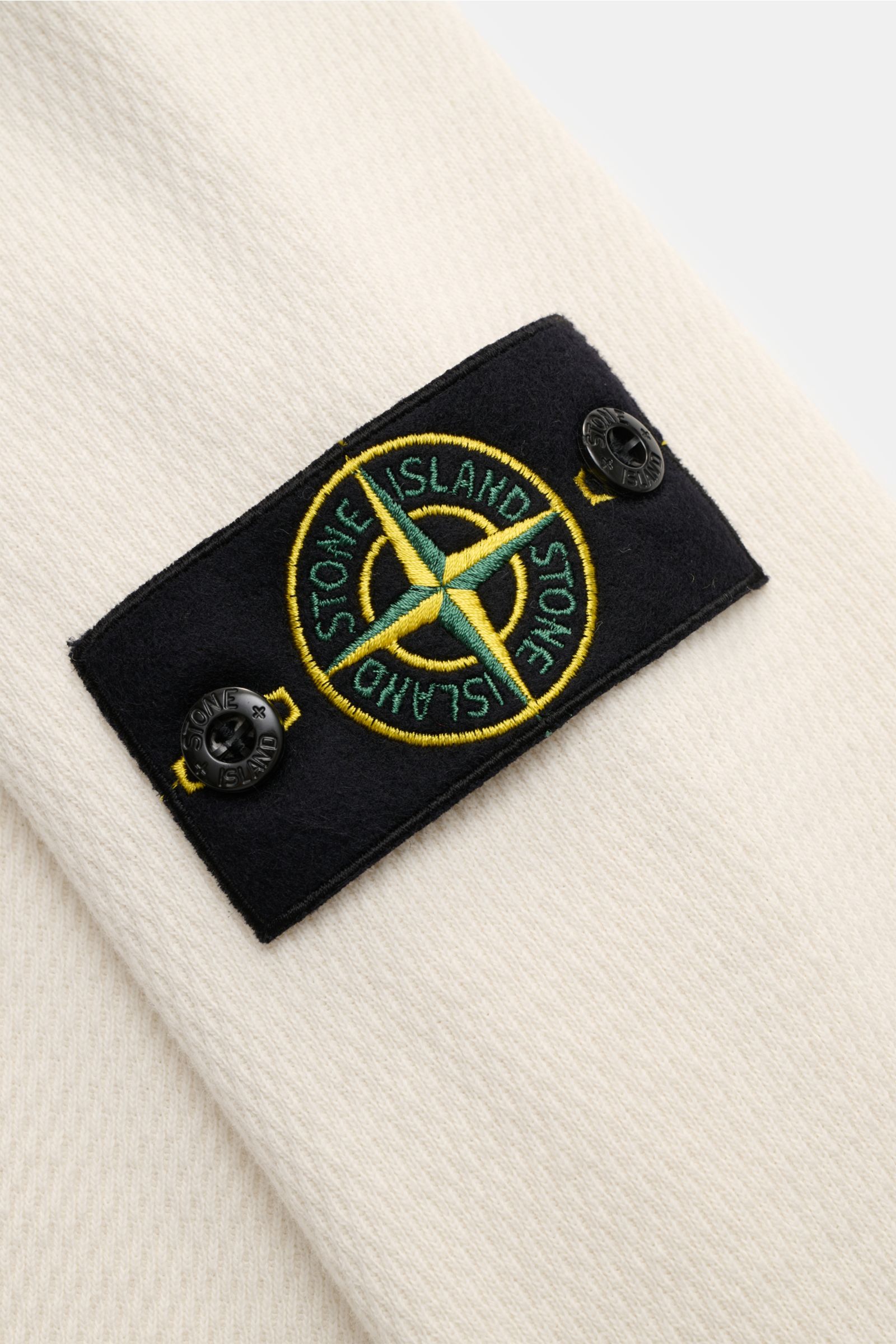 Stone Island Rundhalspullover creme aus reiner Baumwolle, strukturierter Jersey mit Overlock-Nähten und Kompass-Badge am Oberarm, Nahaufnahme.