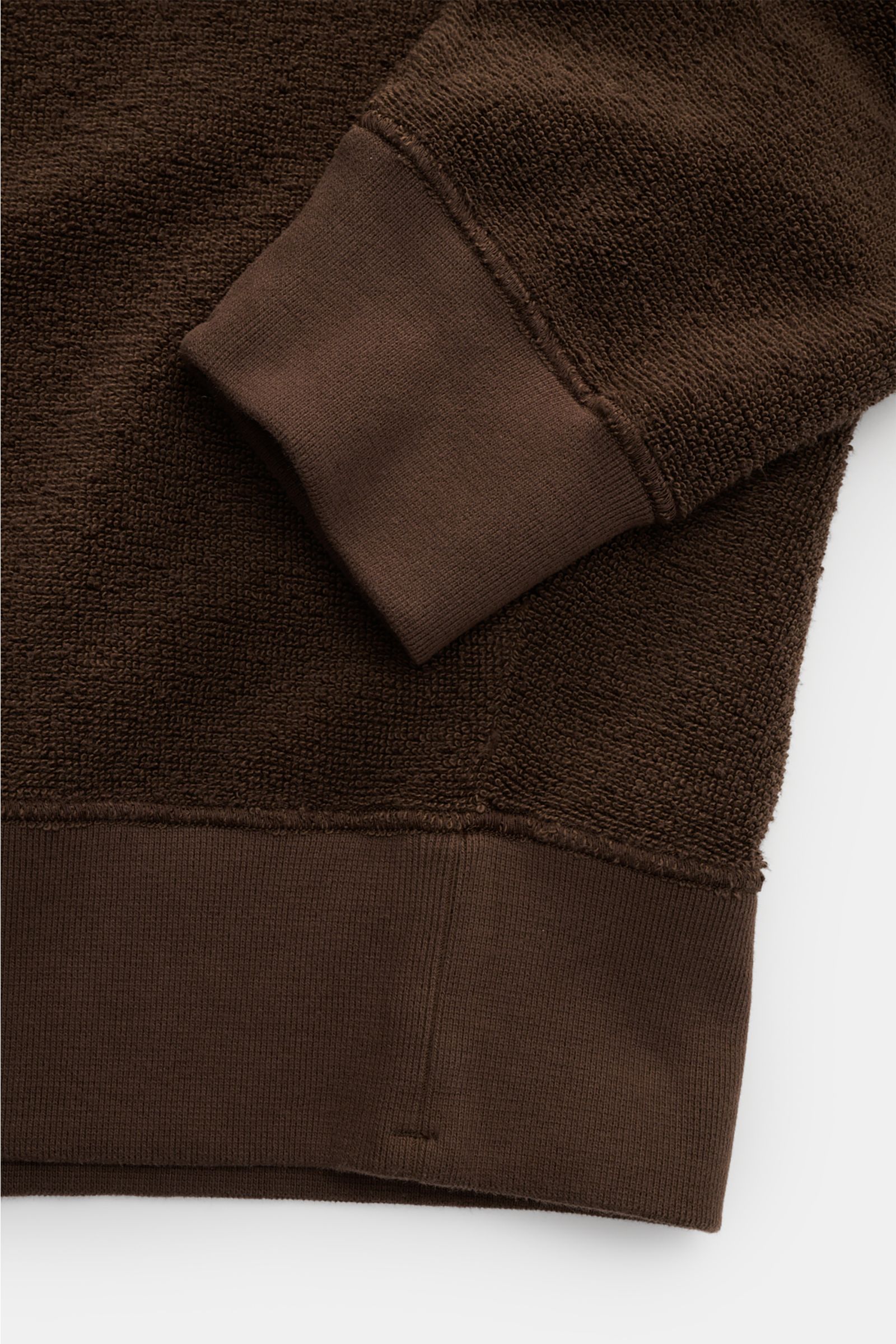 Nahaufnahme des Stone Island Frottee-Rundhals-Sweatshirts dunkelbraun, detailreich von unten rechts fotografiert, zeigt Raglanärmel, breite Rippbündchen und die schwere Baumwolle-Microfaser-Qualität.