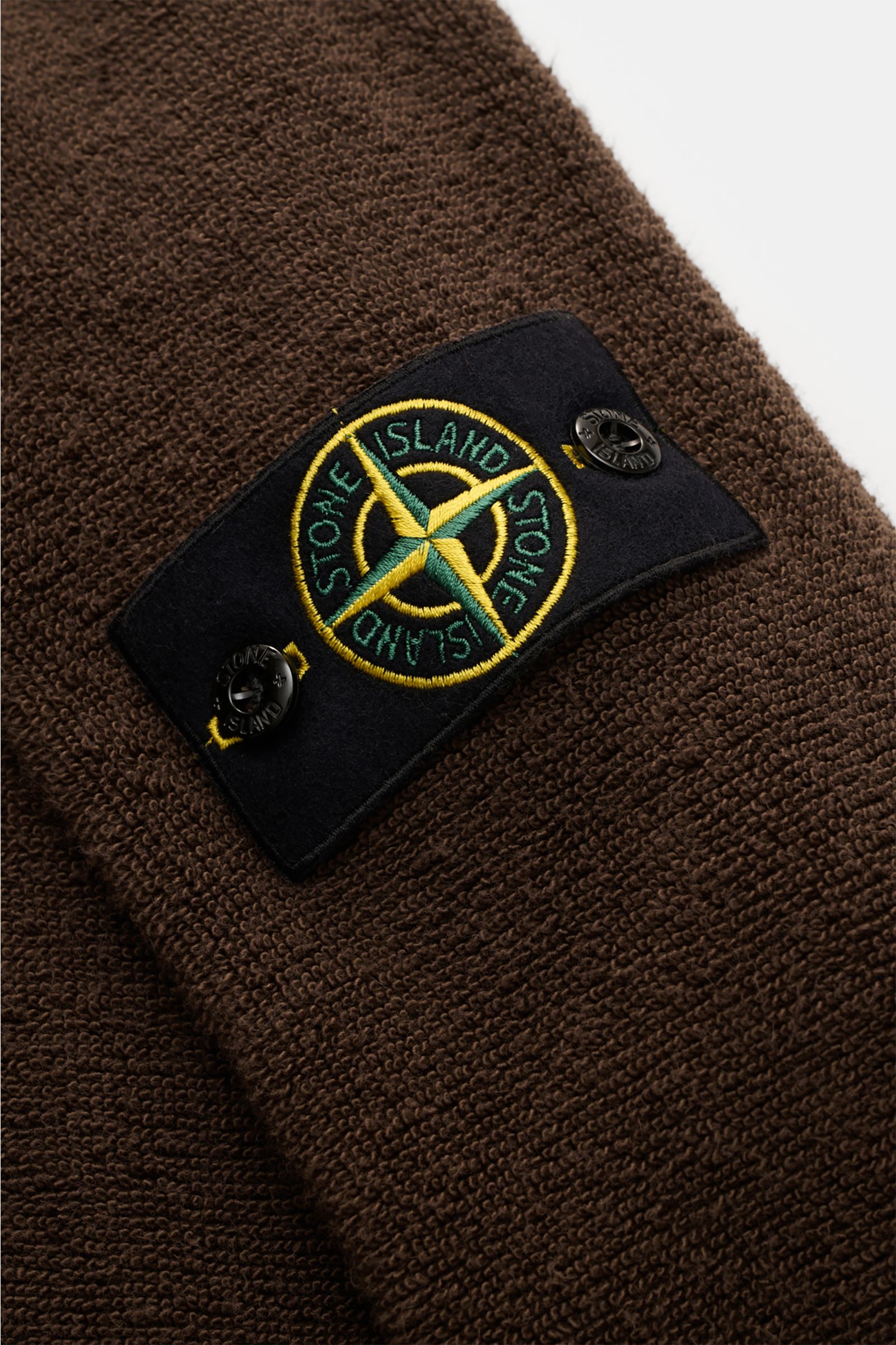 Nahaufnahme des Stone Island Frottee-Rundhals-Sweatshirts dunkelbraun mit schwerem Baumwolle-Microfaser-Mix, ikonischem Kompass-Badge und grober Frottee-Struktur, fotografiert schräg von oben.