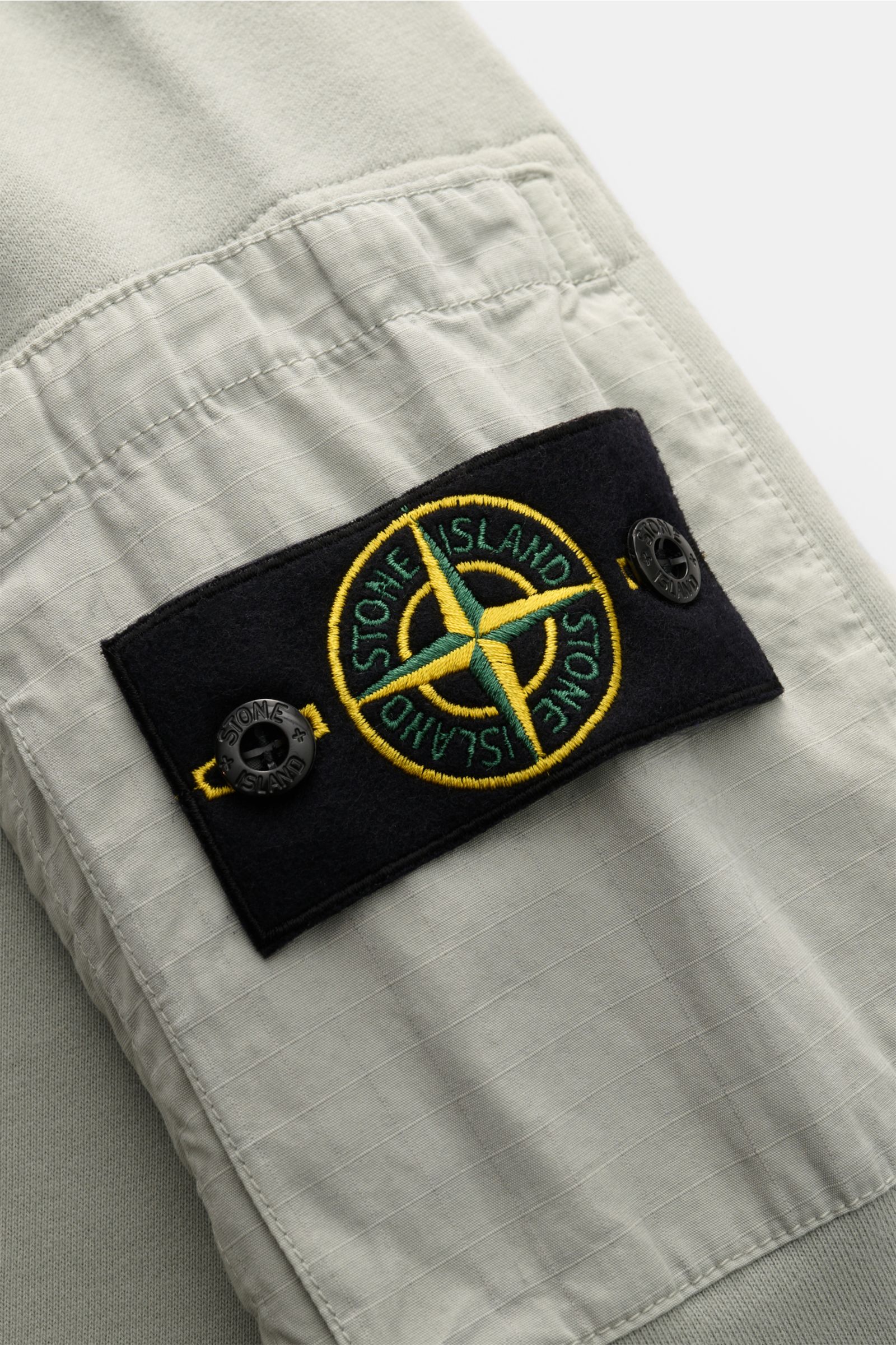 Nahaufnahme des Stone Island Rundhals-Sweatshirts 'Seasonal Pocket' salbei, Fokus auf Tasche mit Kompass-Badge am Oberarm, weicher Baumwollstoff, Rippbündchen, Regular Fit.