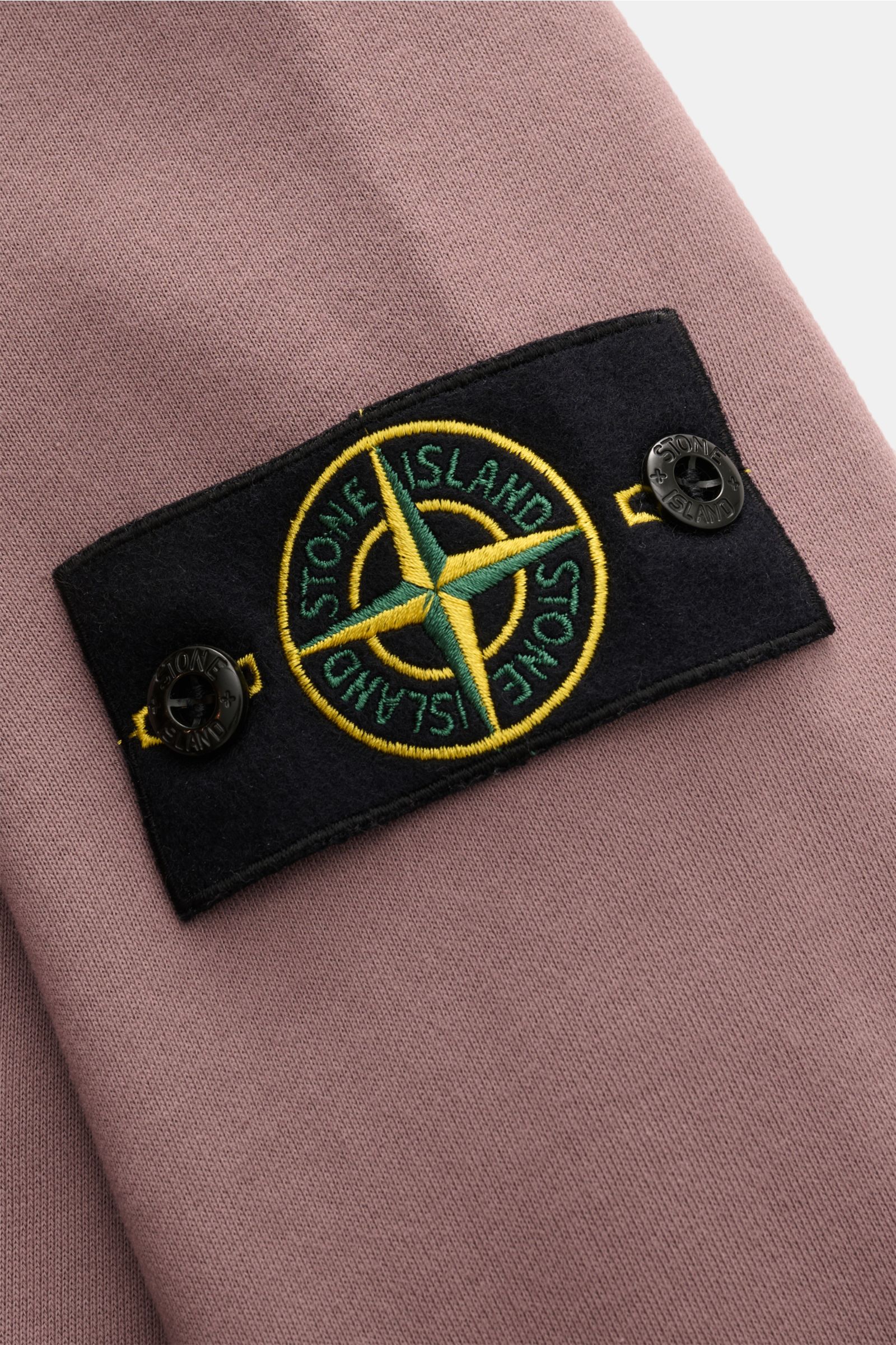 Close-up front-side view of the Stone Island Rundhals-Sweatshirt 'Basic Sweat' flieder showing the black compass badge with yellow and green embroidery on lilac cotton fabric.

Zeitloses Basic Piece: Das sportive Sweatshirt von STONE ISLAND wird zur id