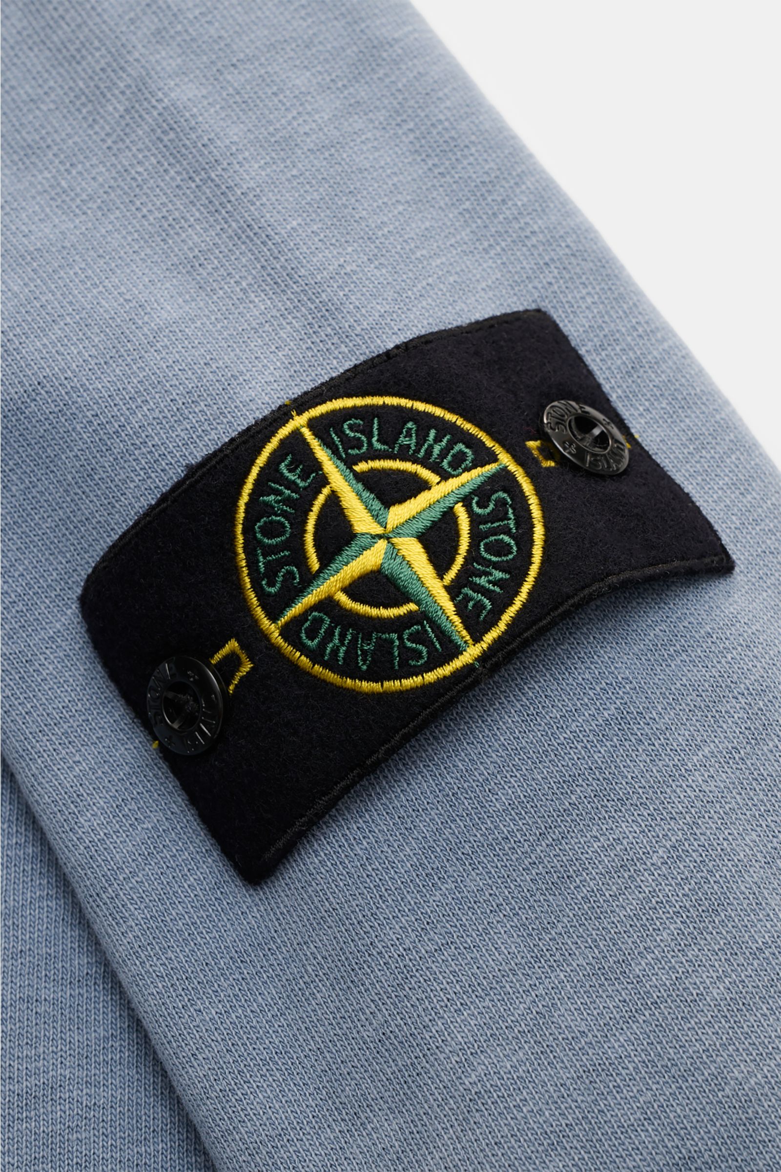 Nahaufnahme aus schräger Perspektive des Stone Island Rundhals-Sweatshirt 'Washed Sweat' graublau mit Kompass-Badge am Oberarm, Baumwolle, weicher Griff, authentischer Washed-Effekt, Regular Fit, Rundhalsausschnitt mit Nahtkante, komfortable Rippbündchen.