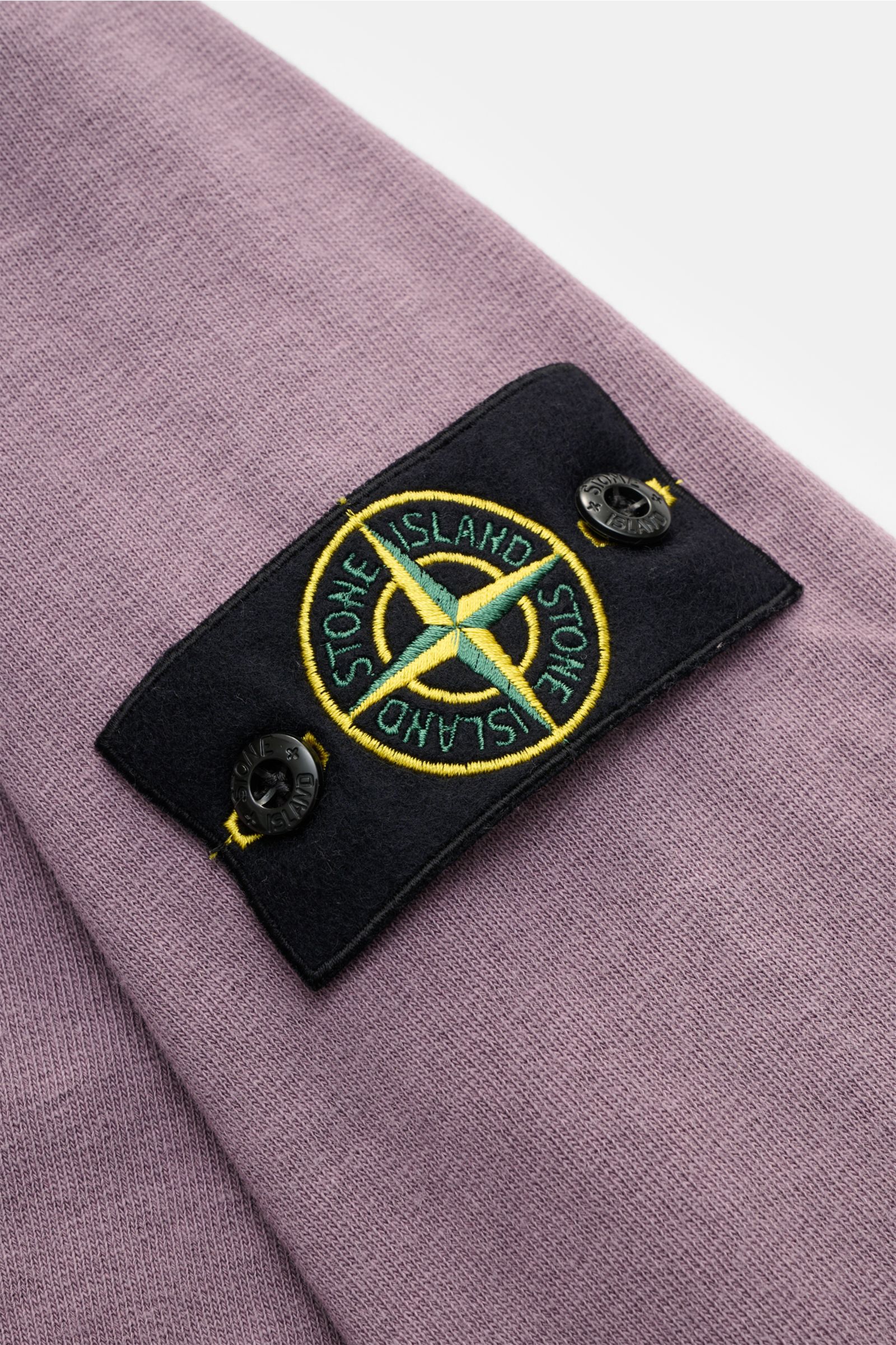 Nahaufnahme des Stone Island Rundhals-Sweatshirts 'Washed Sweat' flieder mit Kompass-Badge am Oberarm, Baumwolle, Washed-Effekt, Nahtkante.