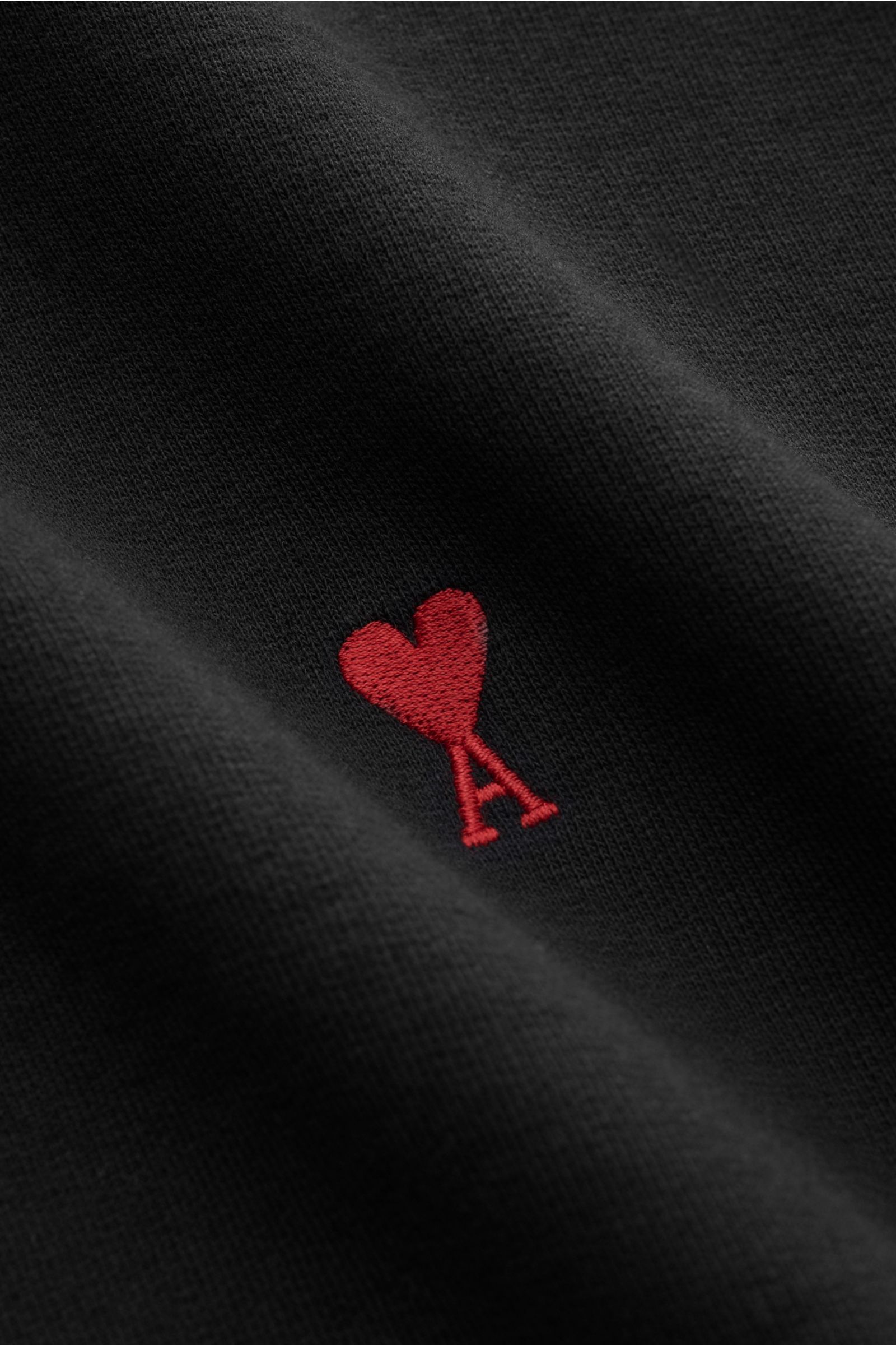 Nahaufnahme des Ami Paris Kapuzenpullover schwarz mit rotem Logo-Stitching auf der Brust, weicher Baumwolle und Regular Fit.