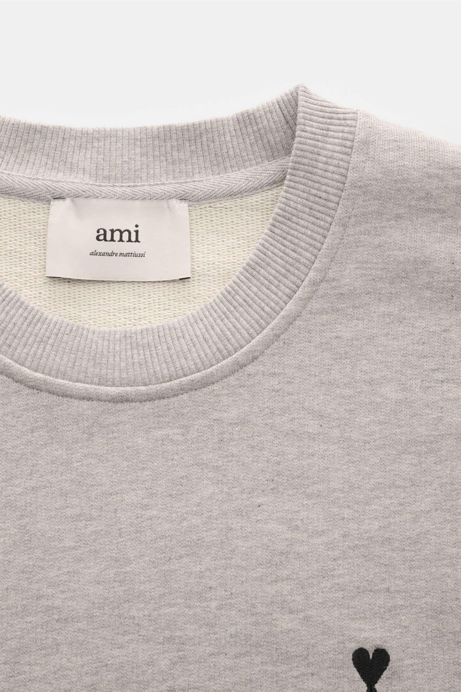 Ami Paris Sweatshirt hellgrau meliert shown from a close-up top-front perspective, featuring a ribbed round neckline, subtle black heart-stitching on the chest, and a visible internal label. Ein dezentes Herz-Stitching auf der Brust verleiht diesem Bau