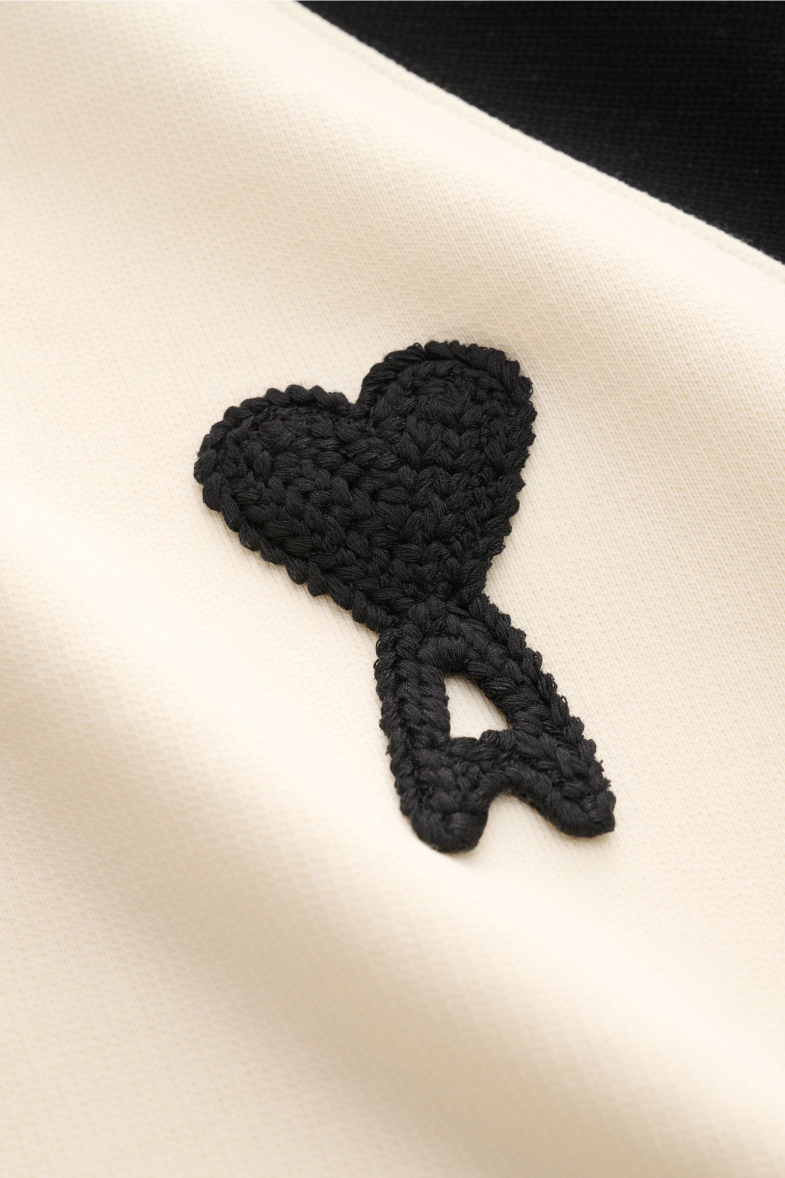 Close-up front view of Ami Paris Sweatshirt 'Boxy Fit Crewneck' creme/schwarz showing black embroidered heart logo on cream fabric. Sportive Raffinesse von AMI PARIS: Die charakteristischen Raglanärmel im Baseballshirt-Stil verleihen dem Sweatshirt ein