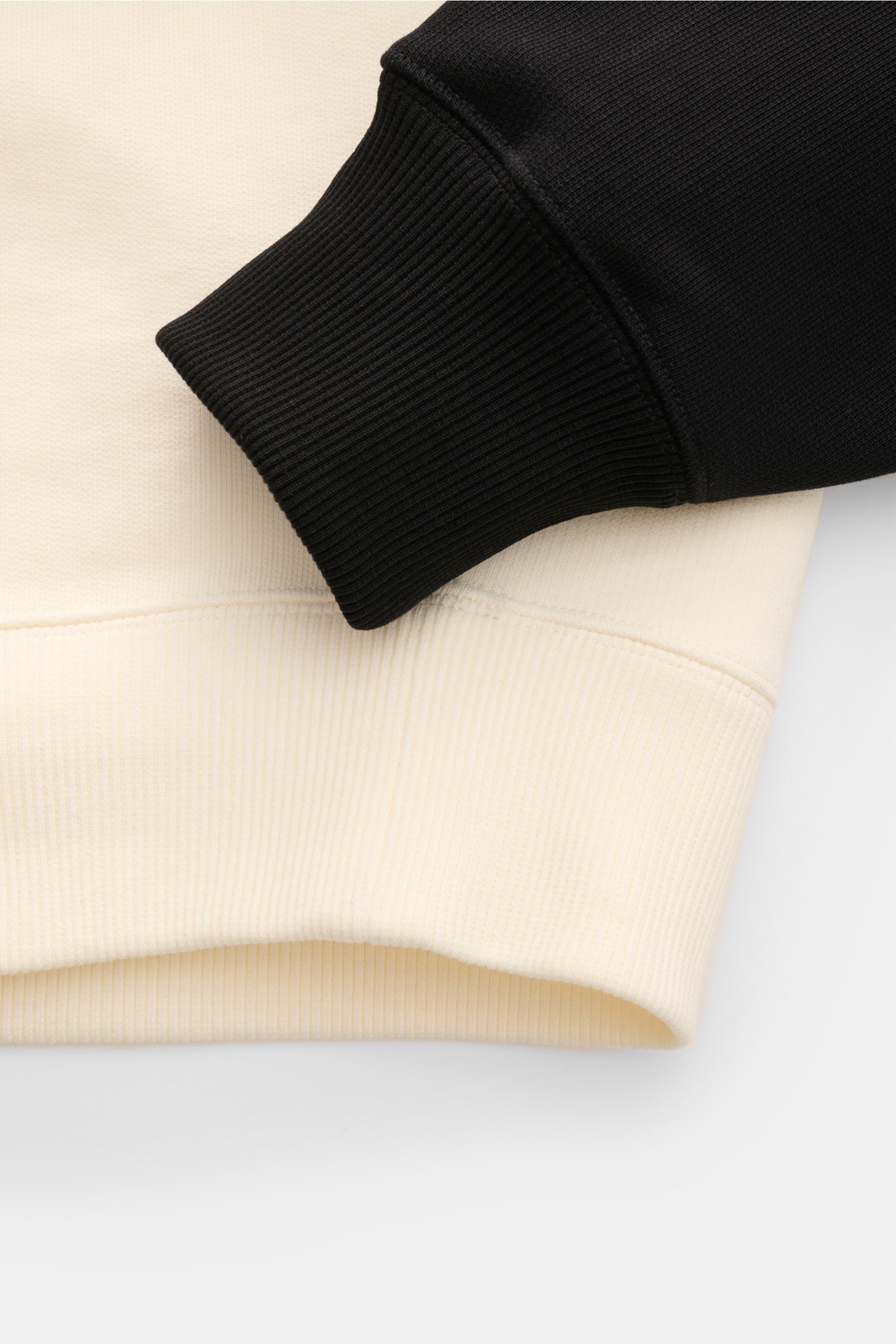 Close-up side view of Ami Paris Sweatshirt 'Boxy Fit Crewneck' creme/schwarz showing black raglan sleeve cuff resting on creme ribbed hem. Sportive Raffinesse von AMI PARIS: Die charakteristischen Raglanärmel im Baseballshirt-Stil verleihen dem Sweatsh