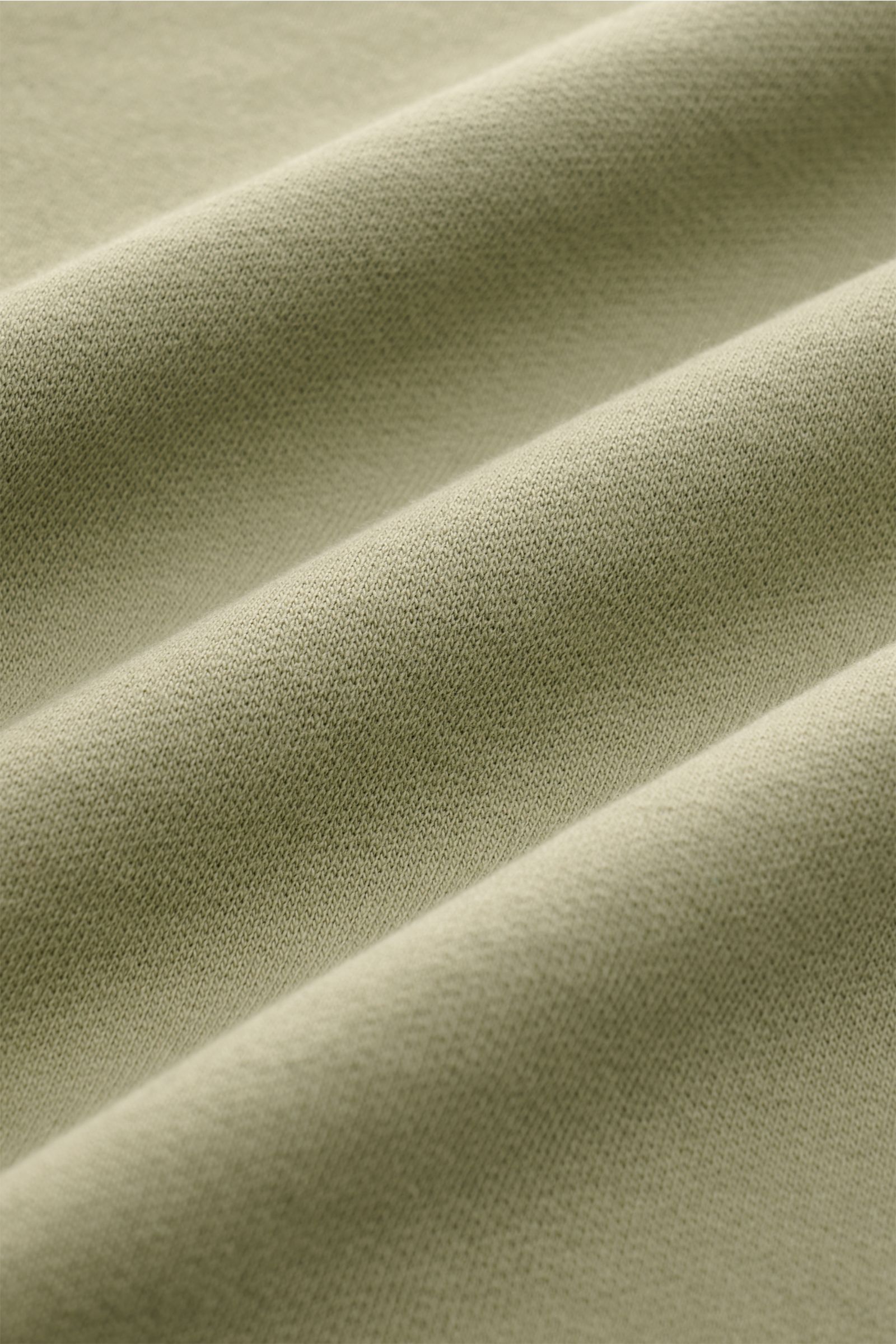 Close-up front view of the olive green C.P. Company Sweatshirt oliv fabric showing its soft, lightweight, garment-dyed pure cotton texture with fine knit detail and slight folds. 