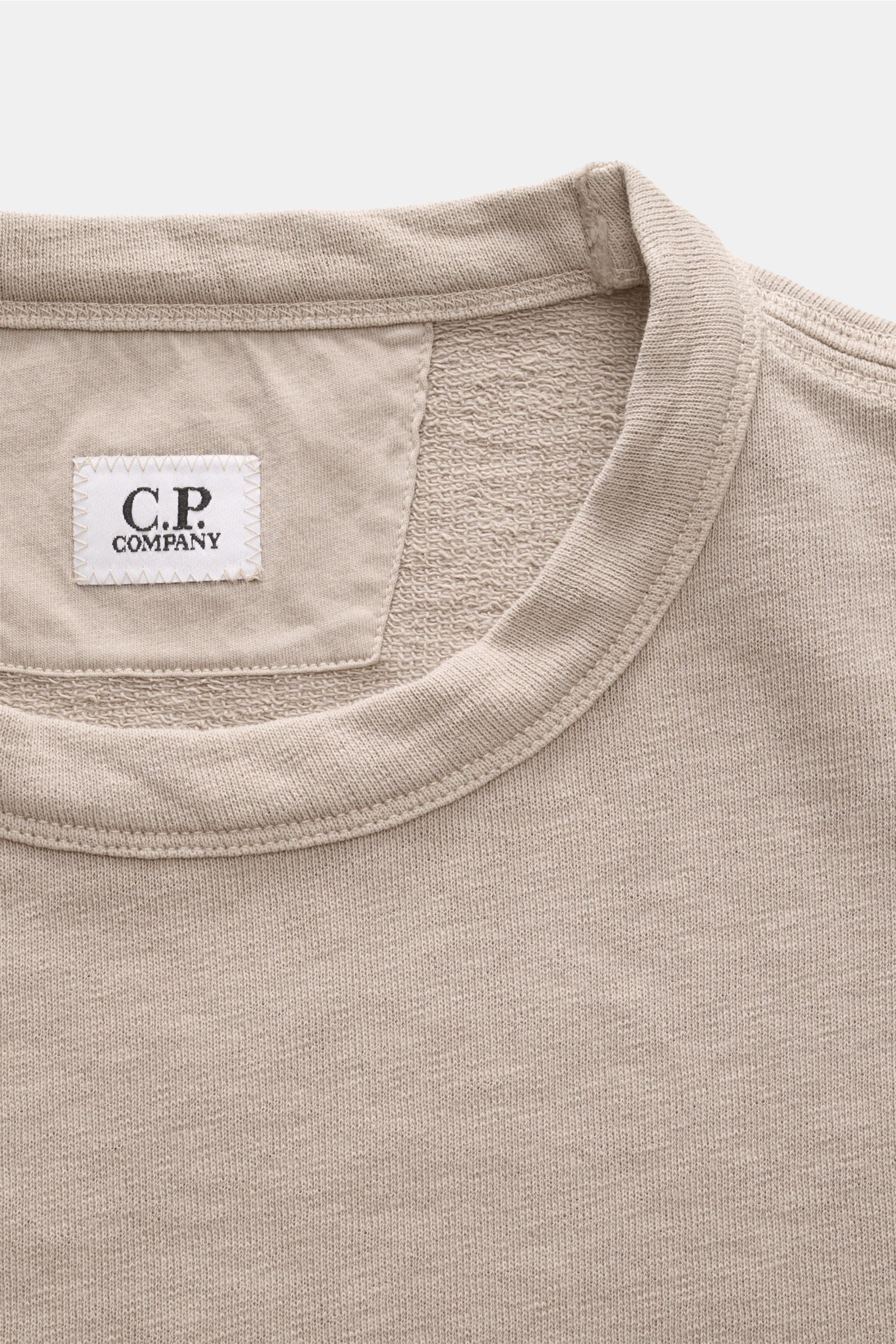C.P. Company Rundhals-Sweatshirt beige shown from a close-up front perspective focusing on the collar, label, and textured cotton fabric. 