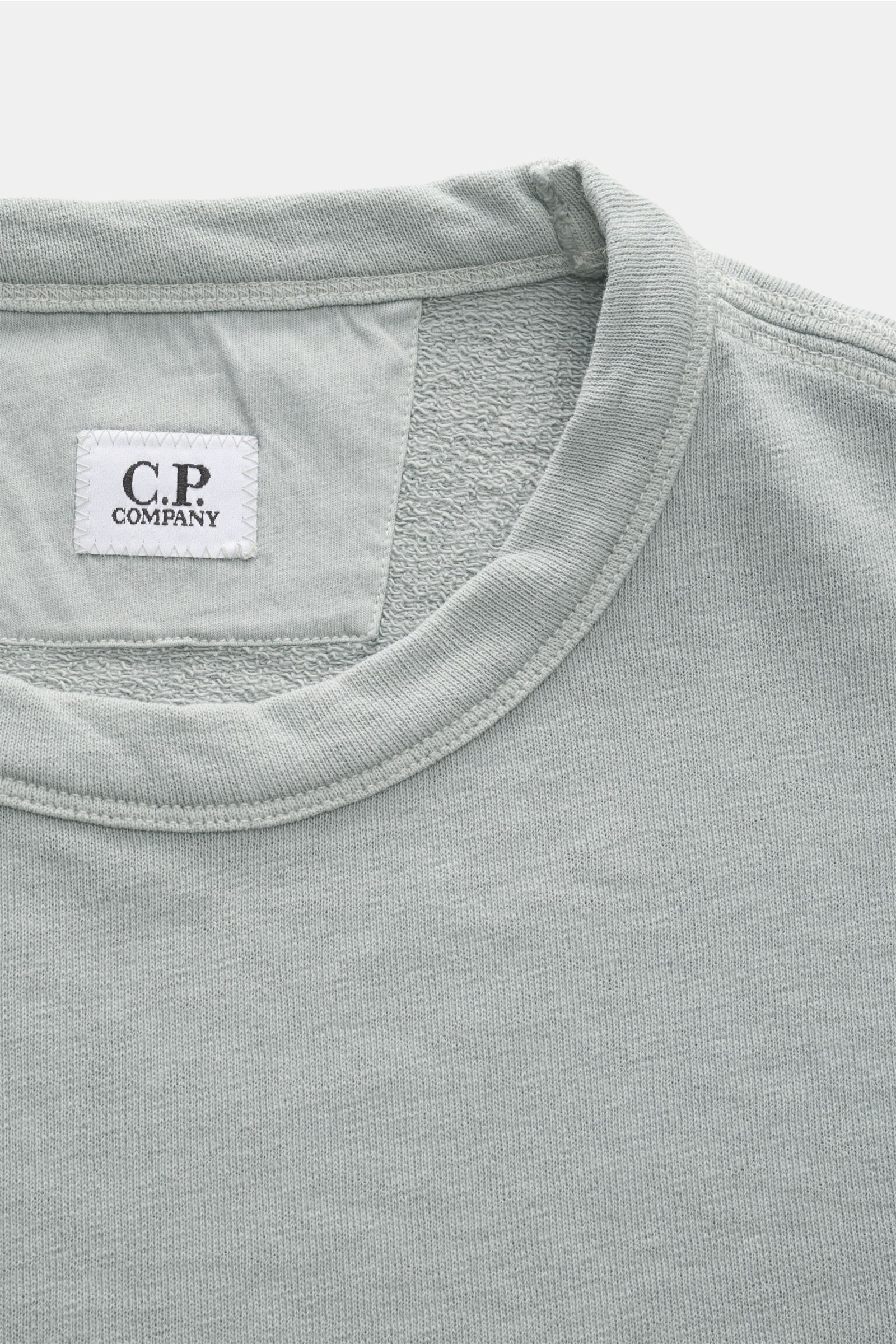 Close-up front view of the collar and inner label of the C.P. Company Crew neck sweatshirt grey-green, featuring lightweight, garment-dyed cotton fabric.


