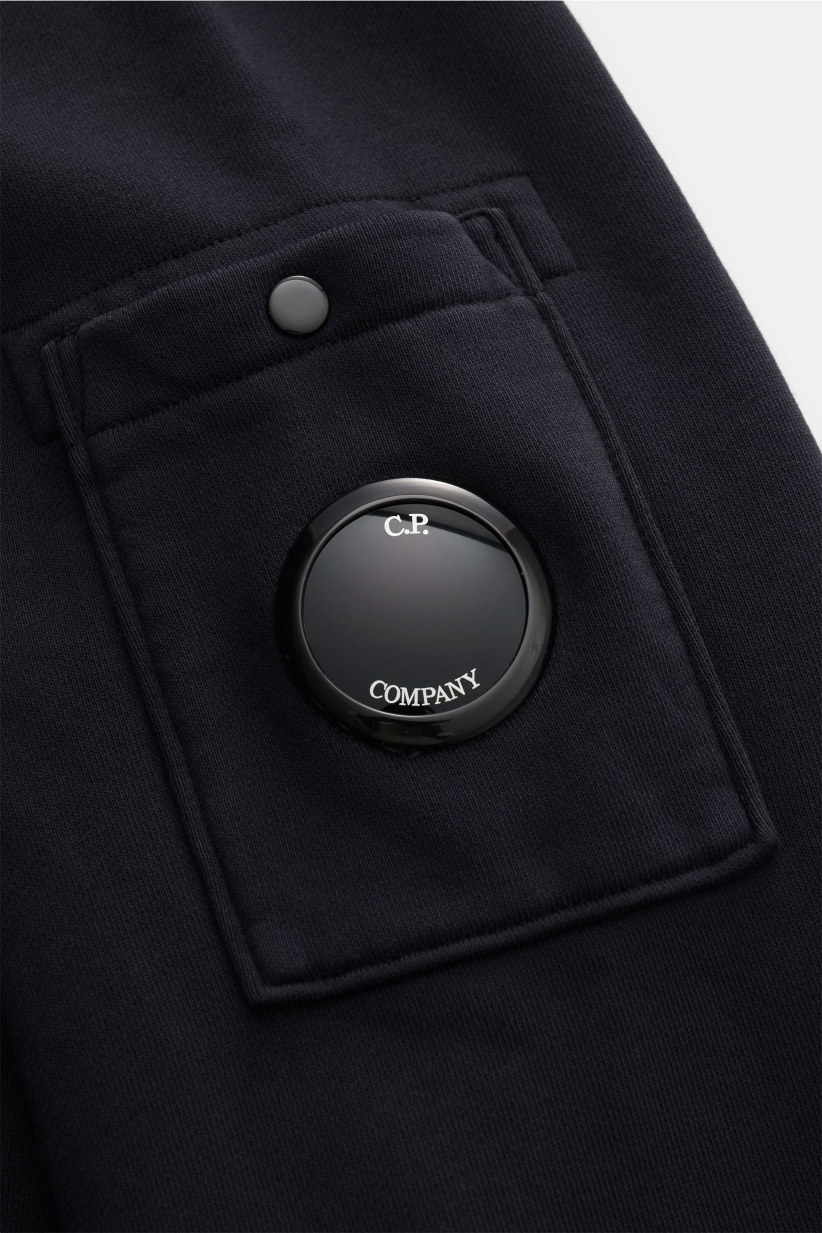 Close-up front-side view of the navy C.P. Company Hooded jumper navy sleeve pocket showing pure cotton fabric, signature lens detail, and snap button. 