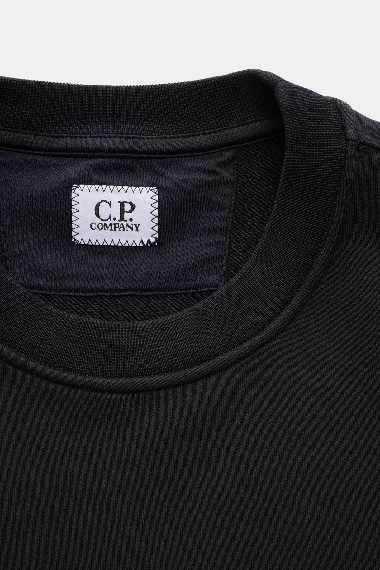 Nahaufnahme des Rundhalsausschnitts und C.P. Company-Labels eines navyfarbenen C.P. Company Sweatshirt navy aus reiner Baumwolle.