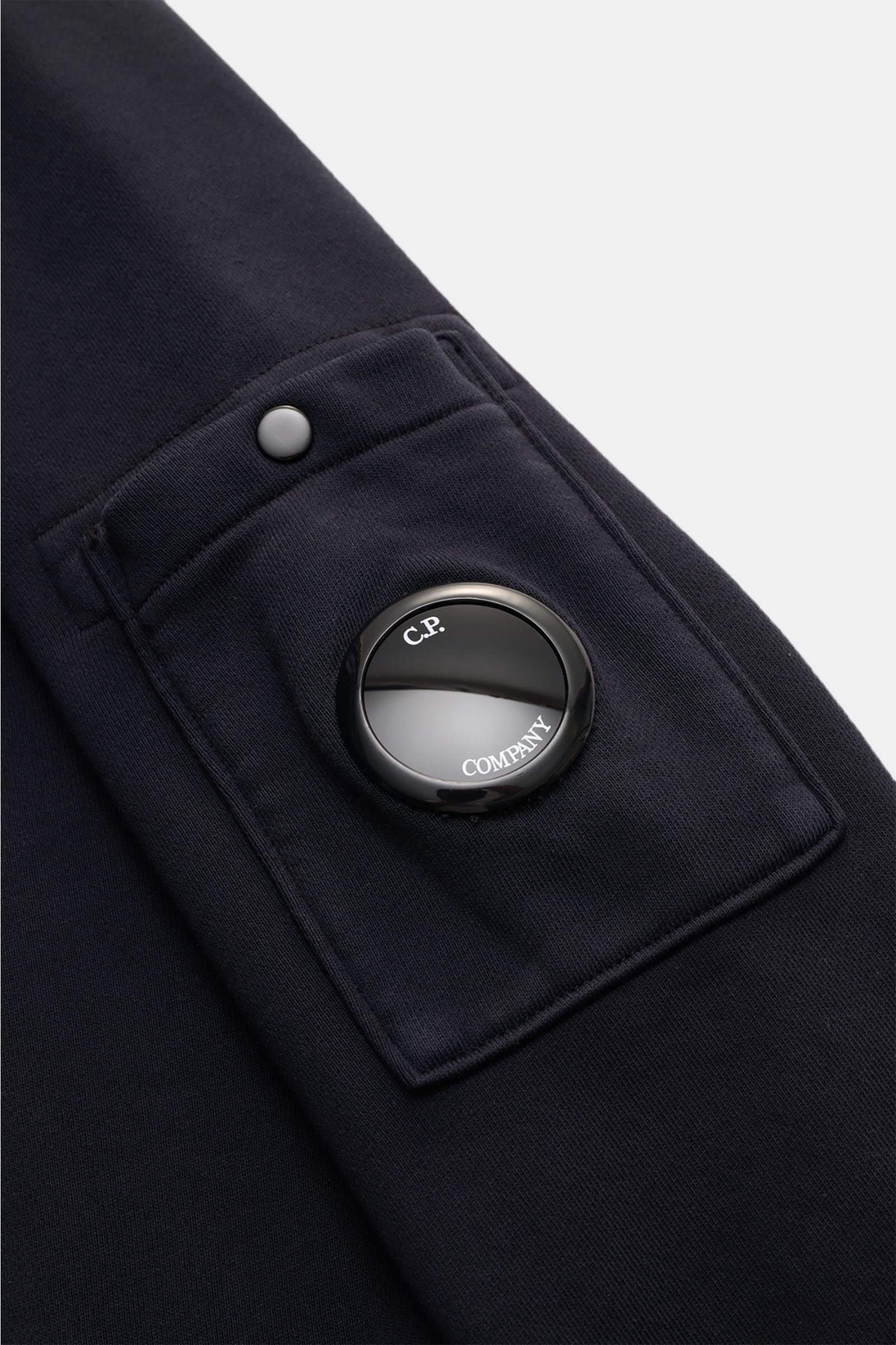 C.P. Company Sweatshirt navy in Nahaufnahme von der Ärmeltasche mit markantem Linsen-Detail und Druckknopf, reine Baumwolle.