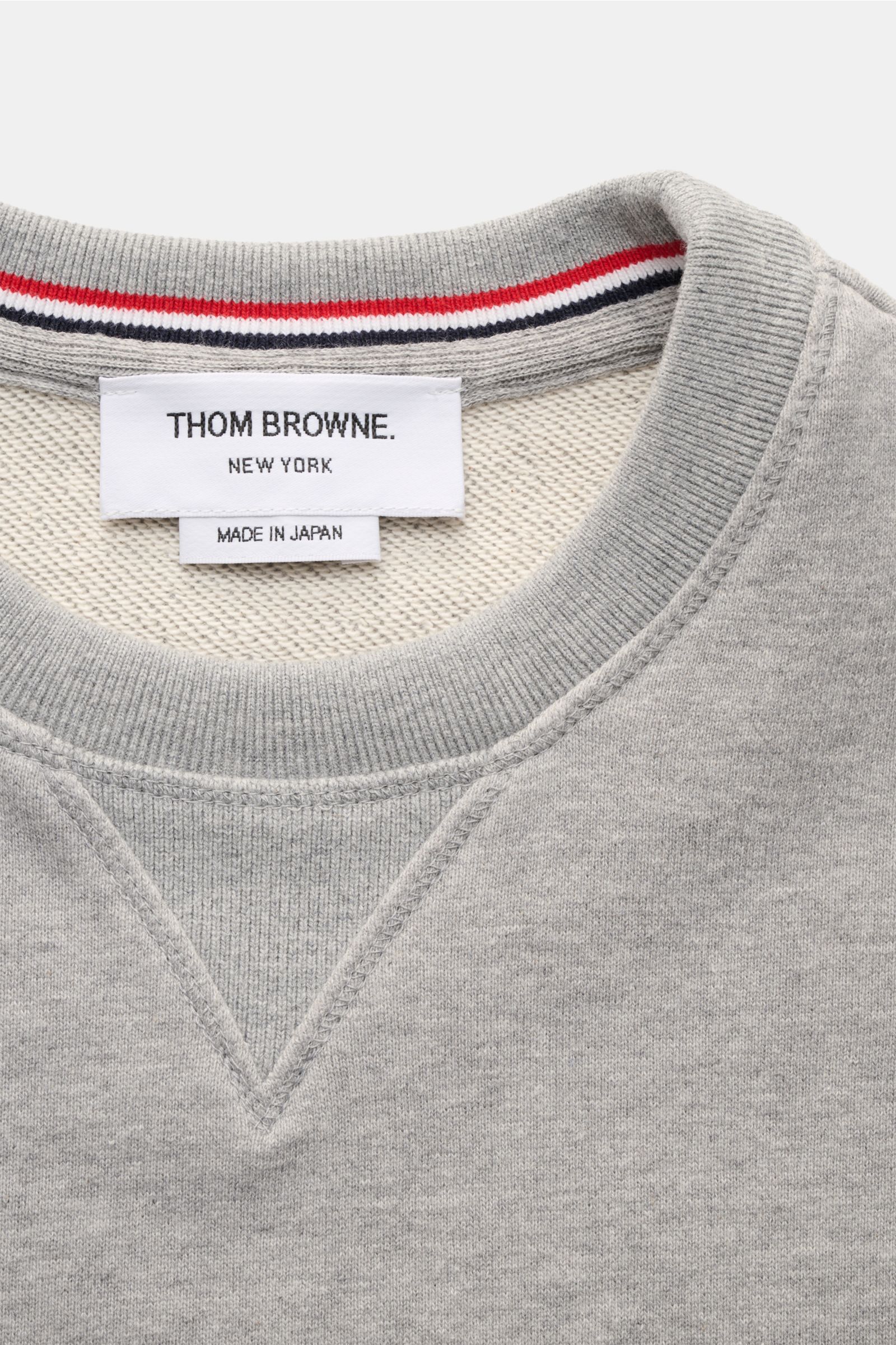 Nahaufnahme des Thom Browne Rundhals-Sweatshirts grau meliert, Perspektive auf Rundhalsausschnitt mit Grosgrain-Schlaufe, weichem Baumwollstoff, Rippbündchen und Kontraststreifen am Ärmel, Regular Fit, sportlich und casual.