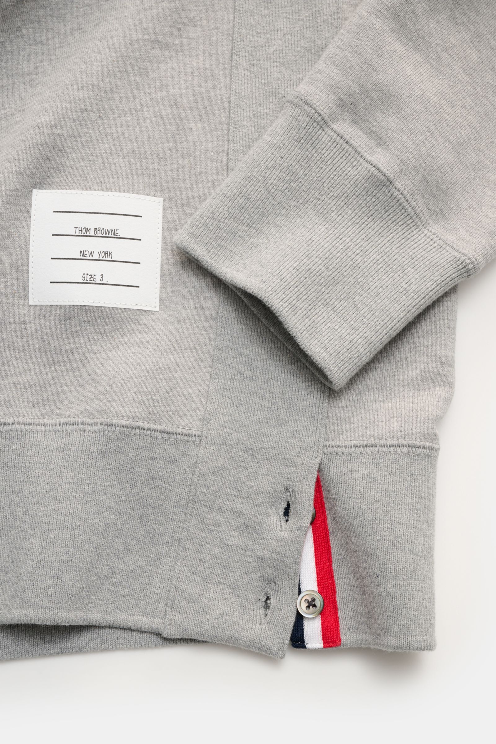 Nahaufnahme des Thom Browne Rundhals-Sweatshirts grau meliert von der Ärmel- und Saumseite, aus reiner Baumwolle mit weichem Griff, Rippbündchen, geknöpften Saumschlitzen mit Grosgrain-Besatz und labeltypischen Kontraststreifen am Ärmel, inklusive rückwär