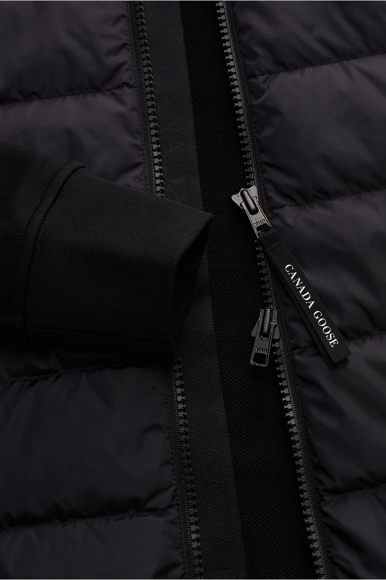 Close-up front view of the Canada Goose Sweatjacke 'HyBridge Huron' schwarz showing black quilted, down-filled front with a robust two-way zipper, soft black cotton sweat raglan sleeve, and ribbed cuff. CANADA GOOSE combines a comfortable cut with raglan 