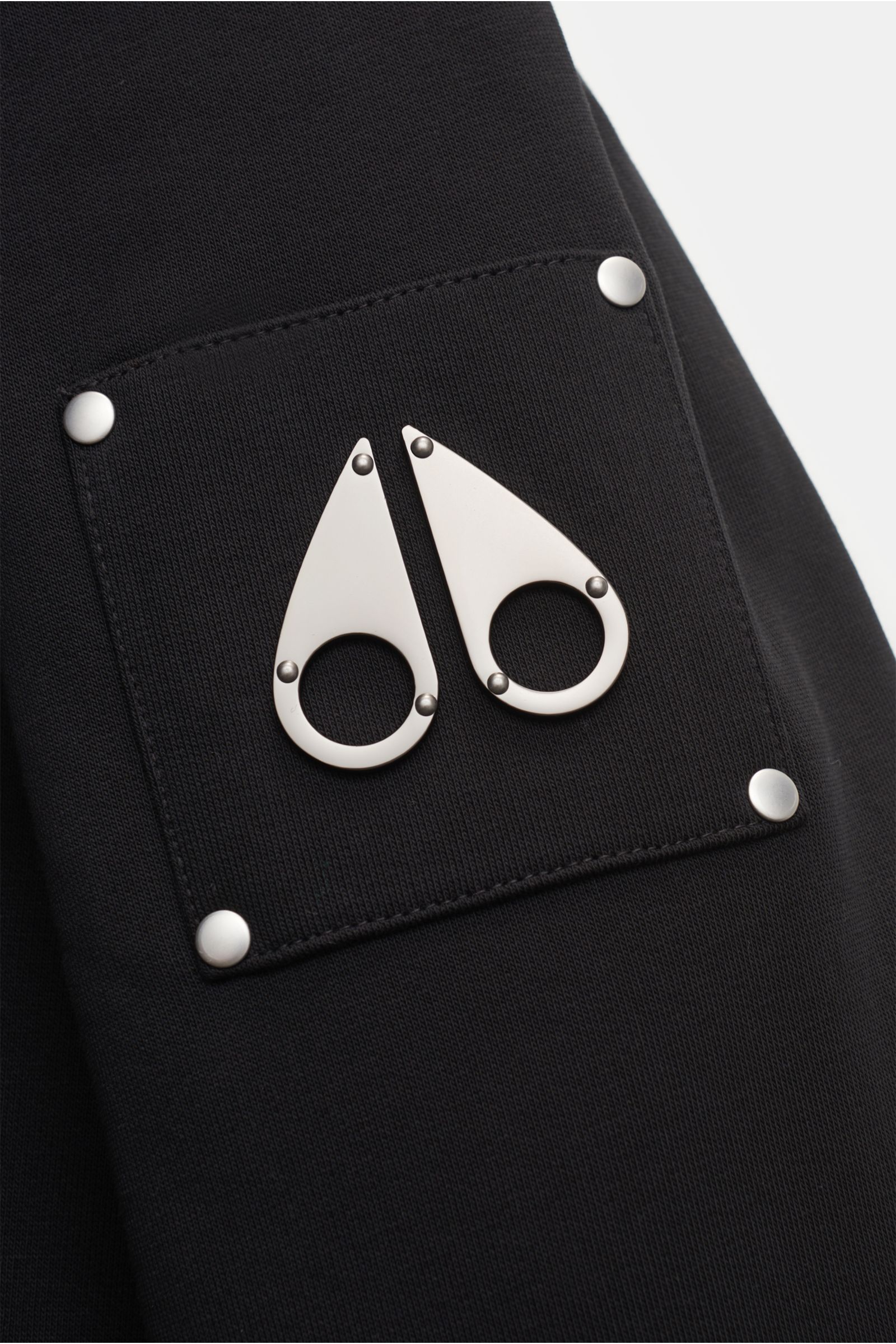 Close-up from a front side view of the Moose Knuckles Sweatjacke 'Classic Bunny' schwarz showing the black fabric and metallic logo patch on the sleeve.

Perfekt für kalte Tage: Dank der leichten Wattierung und einer Kapuze mit abnehmbarem Faux-Fur-Inn