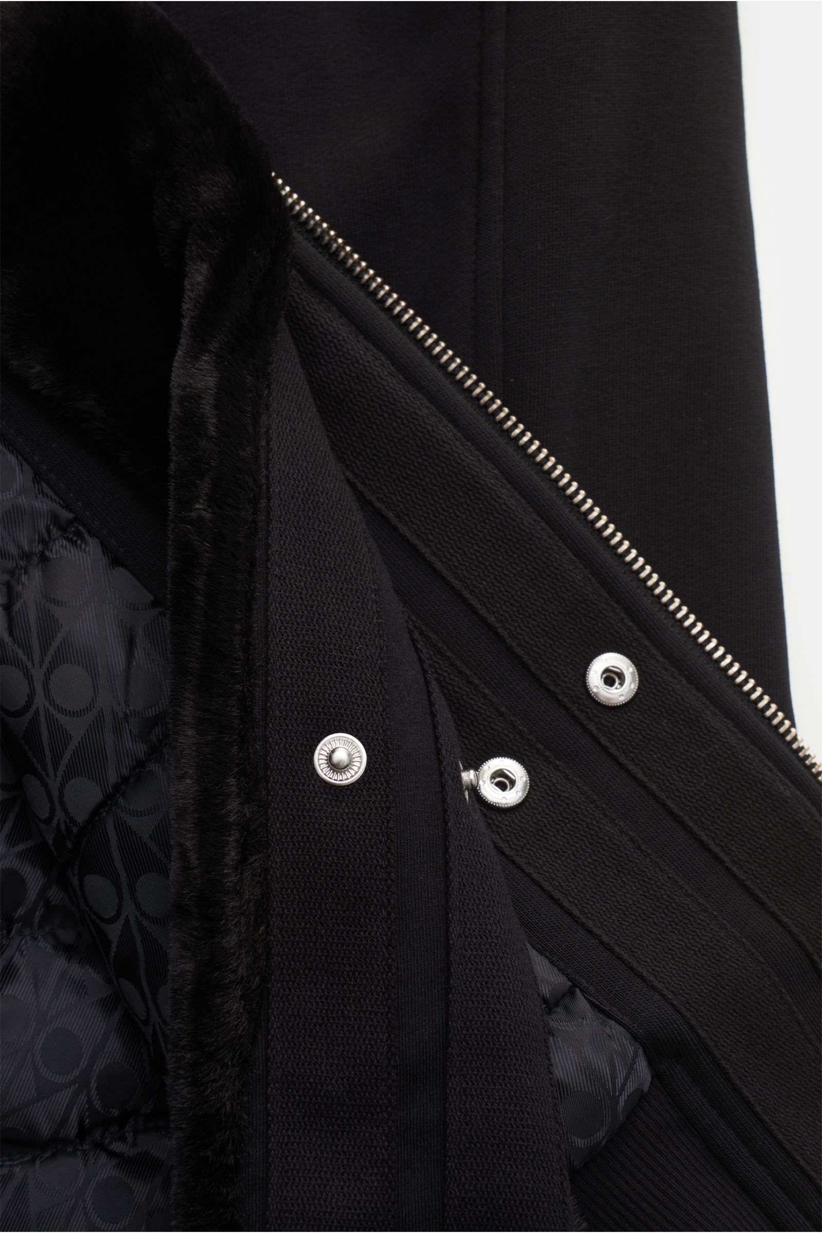Close-up view of the Moose Knuckles Sweatjacke 'Classic Bunny' schwarz showing the black jersey fabric, silver zipper, snap buttons, faux-fur hood lining, and quilted branded inner lining.

Perfekt für kalte Tage: Dank der leichten Wattierung und einer