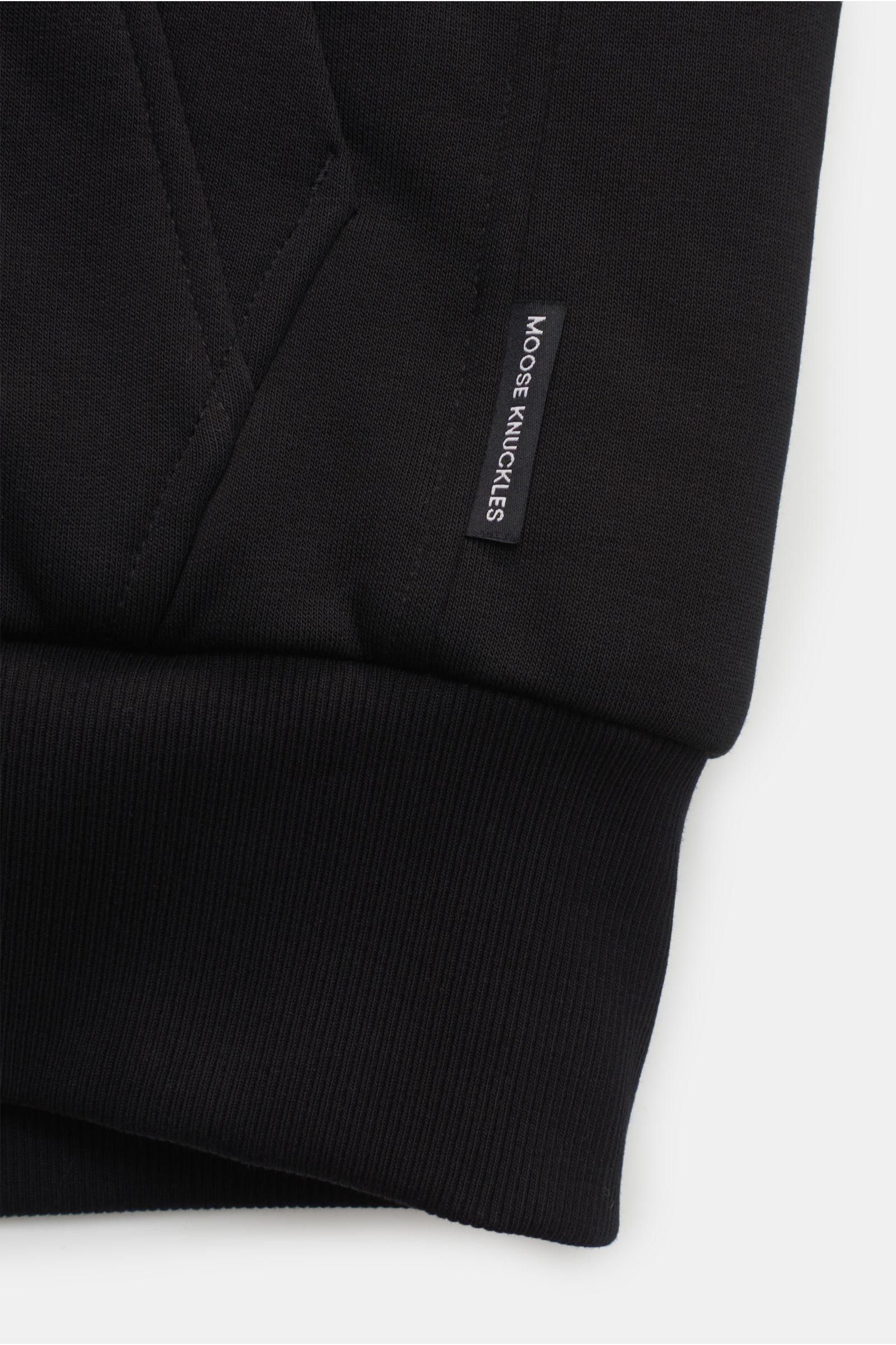 Close-up front view of the sleeve cuff and pocket area of the Moose Knuckles Sweatjacke 'Classic Bunny' schwarz, showing the black jersey fabric, ribbed cuff, and a small 'MOOSE KNUCKLES' label.

Perfekt für kalte Tage: Dank der leichten Wattierung und