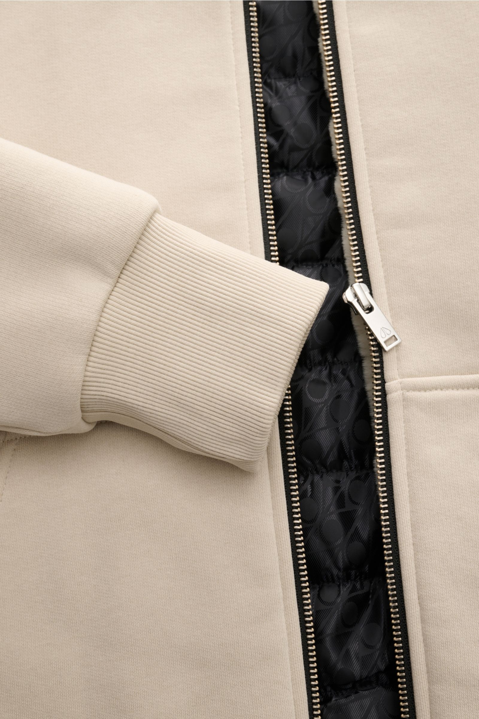 Close-up front view of the Moose Knuckles Sweatjacke 'Classic Bunny' creme showing ribbed cuff, zipper, and branded black quilted lining.

Perfekt für kalte Tage: Dank der leichten Wattierung und einer Kapuze mit abnehmbarem Faux-Fur-Innenfutter sind S