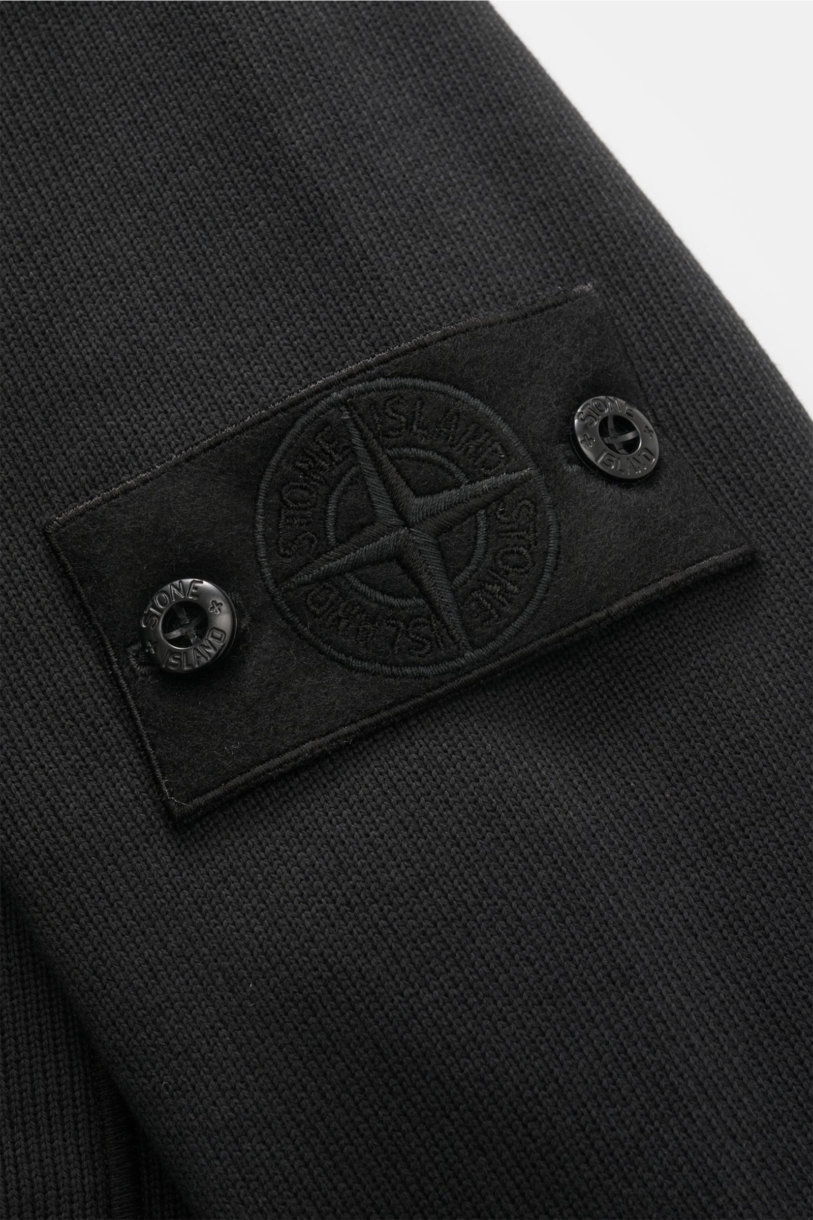 Nahaufnahme der schwarzen Stone Island Sweatjacke 'Ghost' mit markentypischem Kompass-Badge am Ärmel, aus reiner Baumwolle, mittelfeinem Strickbild und Regular Fit.