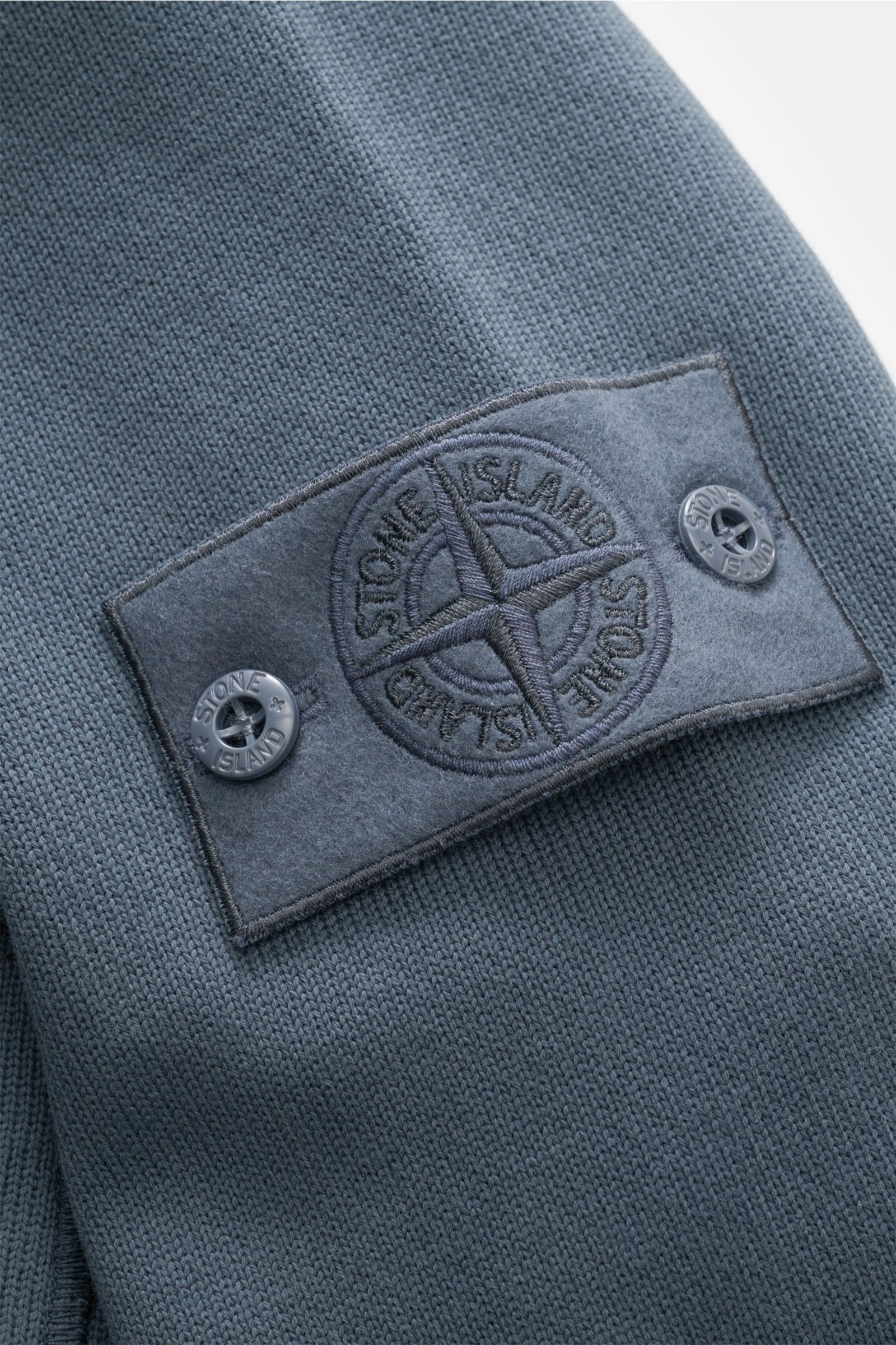 Nahaufnahme der Stone Island Sweatjacke 'Ghost' graublau von der Ärmelperspektive mit markentypischem Kompass-Badge aus reiner Baumwolle.