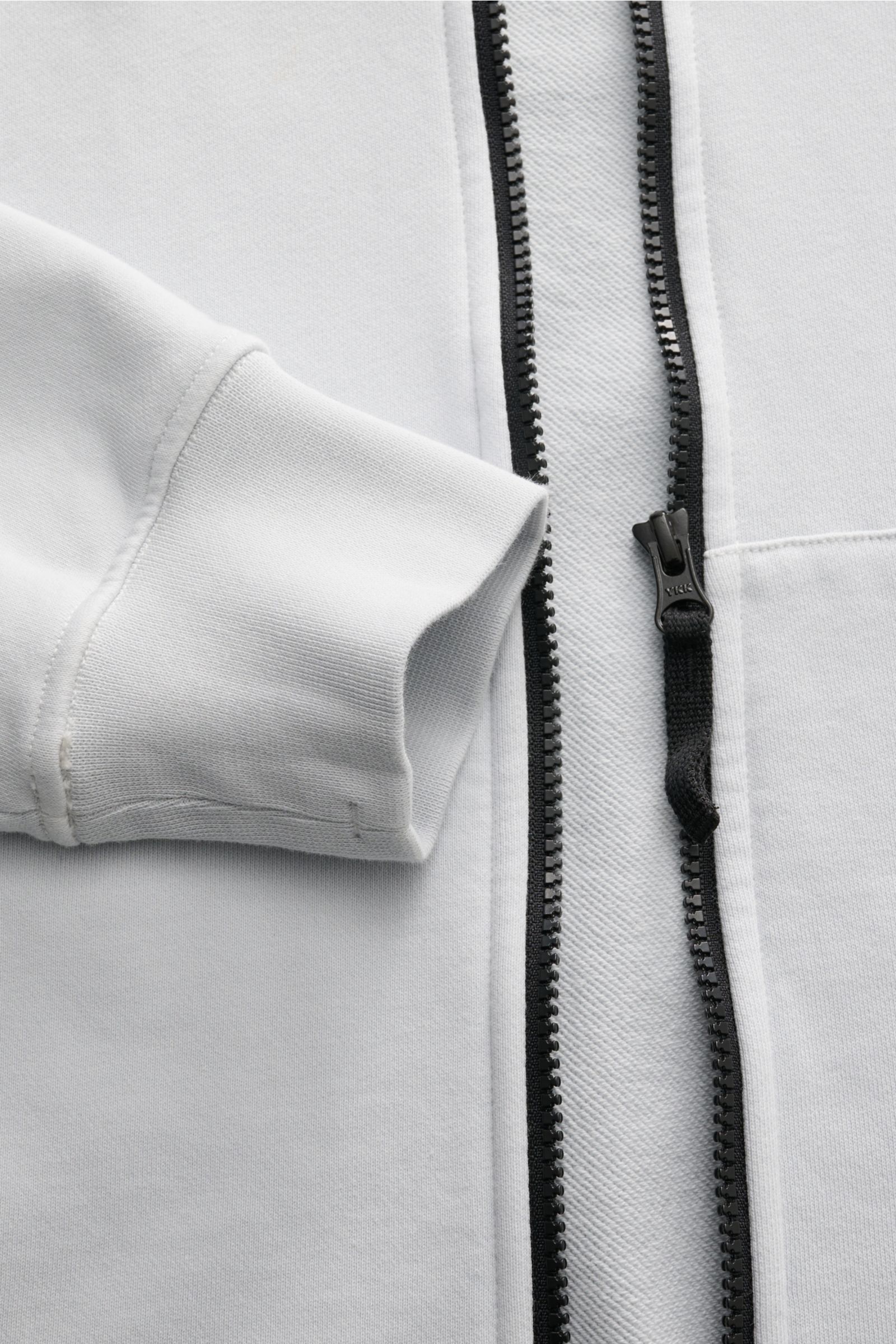 Nahaufnahme der Stone Island Sweatjacke hellgrau von oben mit sichtbarem schwarzen Reißverschluss, weichem Baumwollstoff und Rippbündchen.