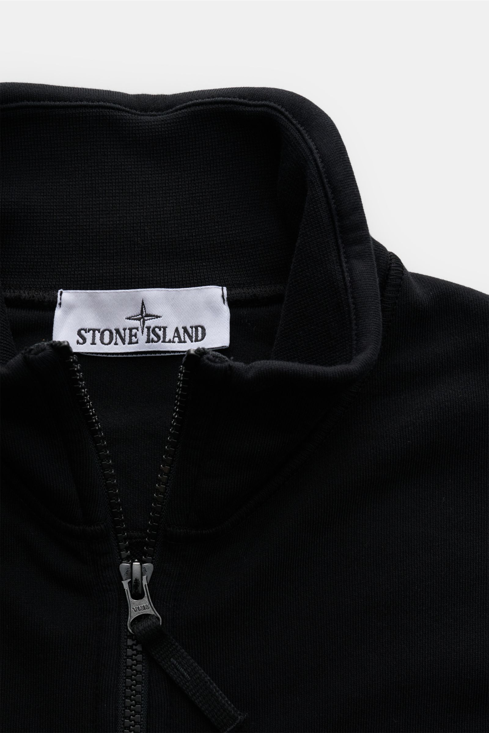 Close-up front view of the Stone Island Sweatjacke schwarz, showing the high collar, robust zipper, and brand label inside the collar. Entspanntes Basic von STONE ISLAND: Mit sportiver Lässigkeit begleitet uns die stückgefärbte Sweatjacke aus softer Ba