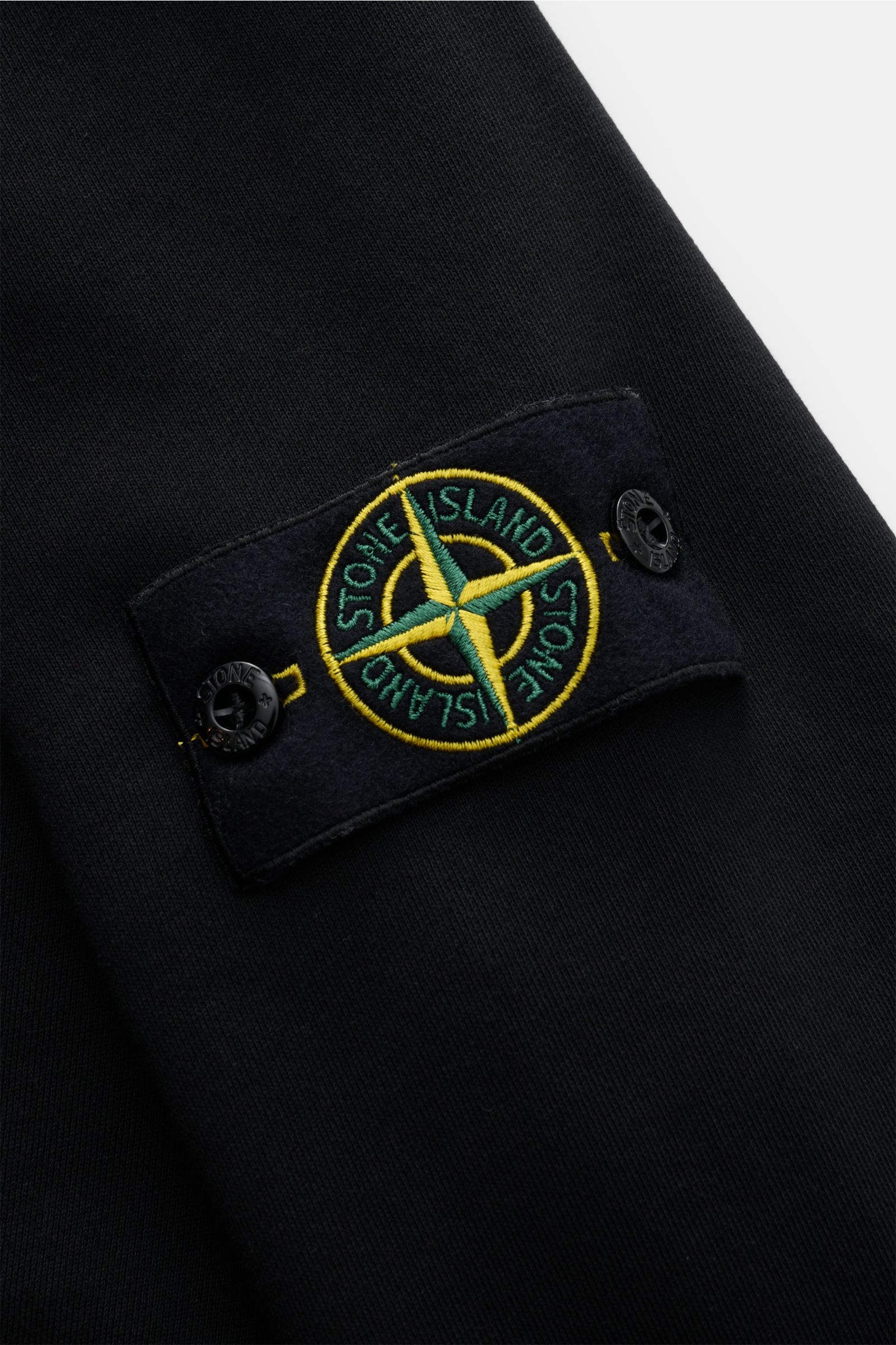 Close-up view of the Stone Island Sweatjacke schwarz sleeve showing the typical compass-badge on soft black cotton fabric.

Entspanntes Basic von STONE ISLAND: Mit sportiver Lässigkeit begleitet uns die stückgefärbte Sweatjacke aus softer Baumwolle bei