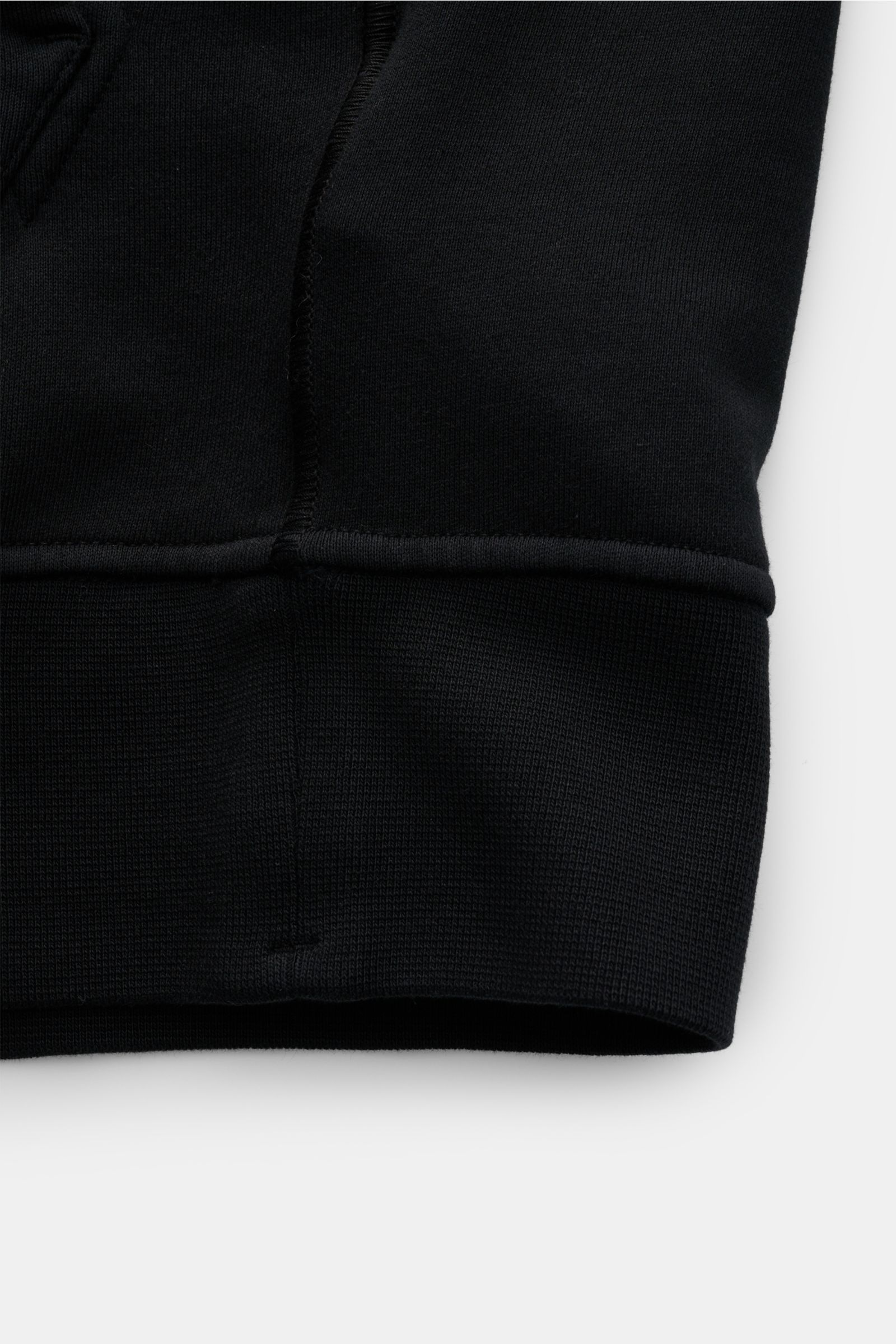 Close-up view of the cuff and hem of the Stone Island Sweatjacke schwarz, showing soft garment-dyed cotton fabric with ribbed cuffs and detailed stitching. Entspanntes Basic von STONE ISLAND: Mit sportiver Lässigkeit begleitet uns die stückgefärbte Swe